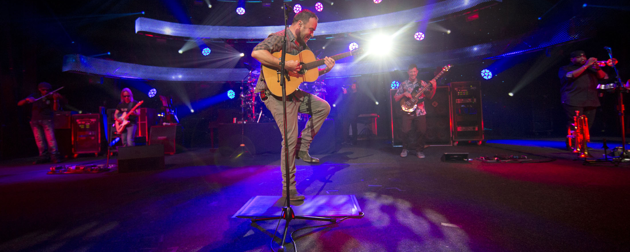 Dave Matthews playing guitar on stage with one leg in the air