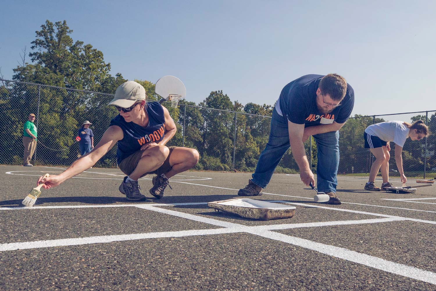 Debbie Mincarelli and Tyler Miller paint lines on an outdoor basketball court