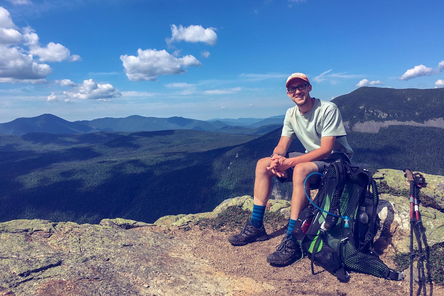 Underhill sits on rocks with his walking sticks and backpack next to him