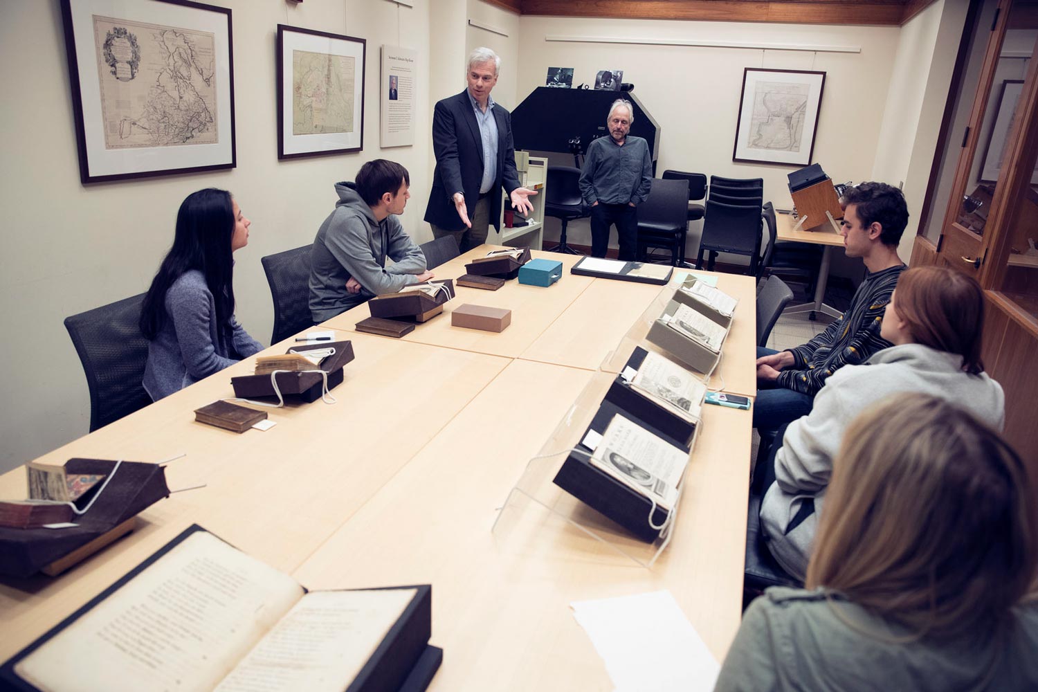 John O’Brien, standing, talking to his students with old books opened on the table