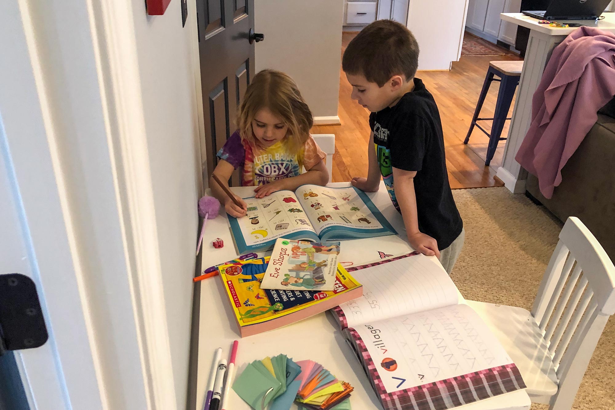 Two children at a small table working together on a homework book