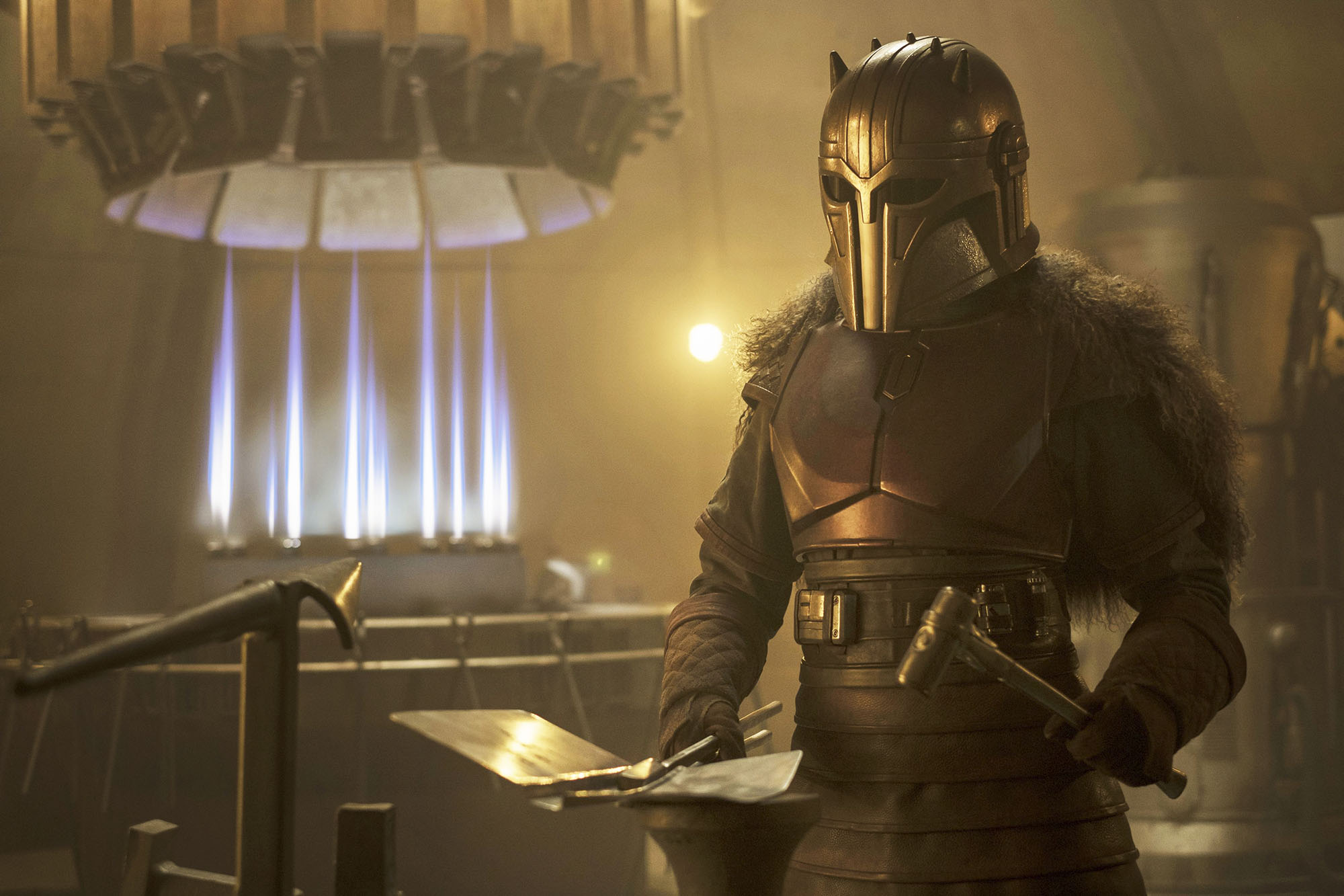 The Armorer dressed in plated metal and a full helmet in the Mandalorian