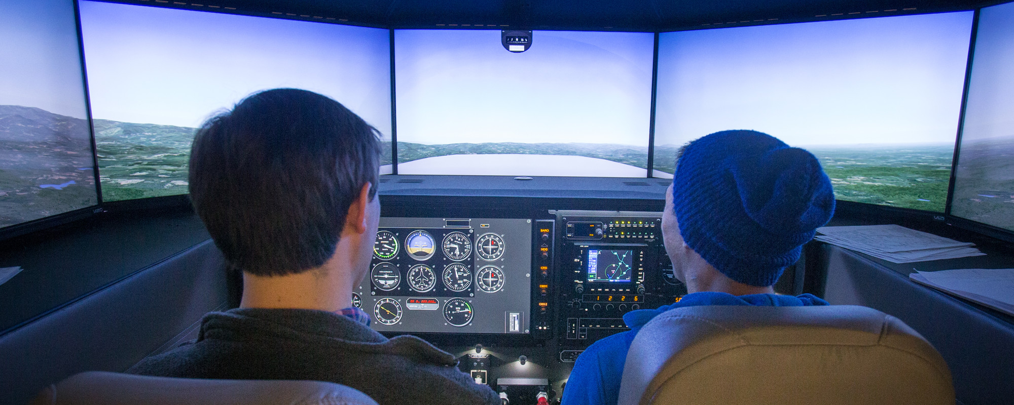 Two people sit in a cockpit of a plane as they fly a simulator