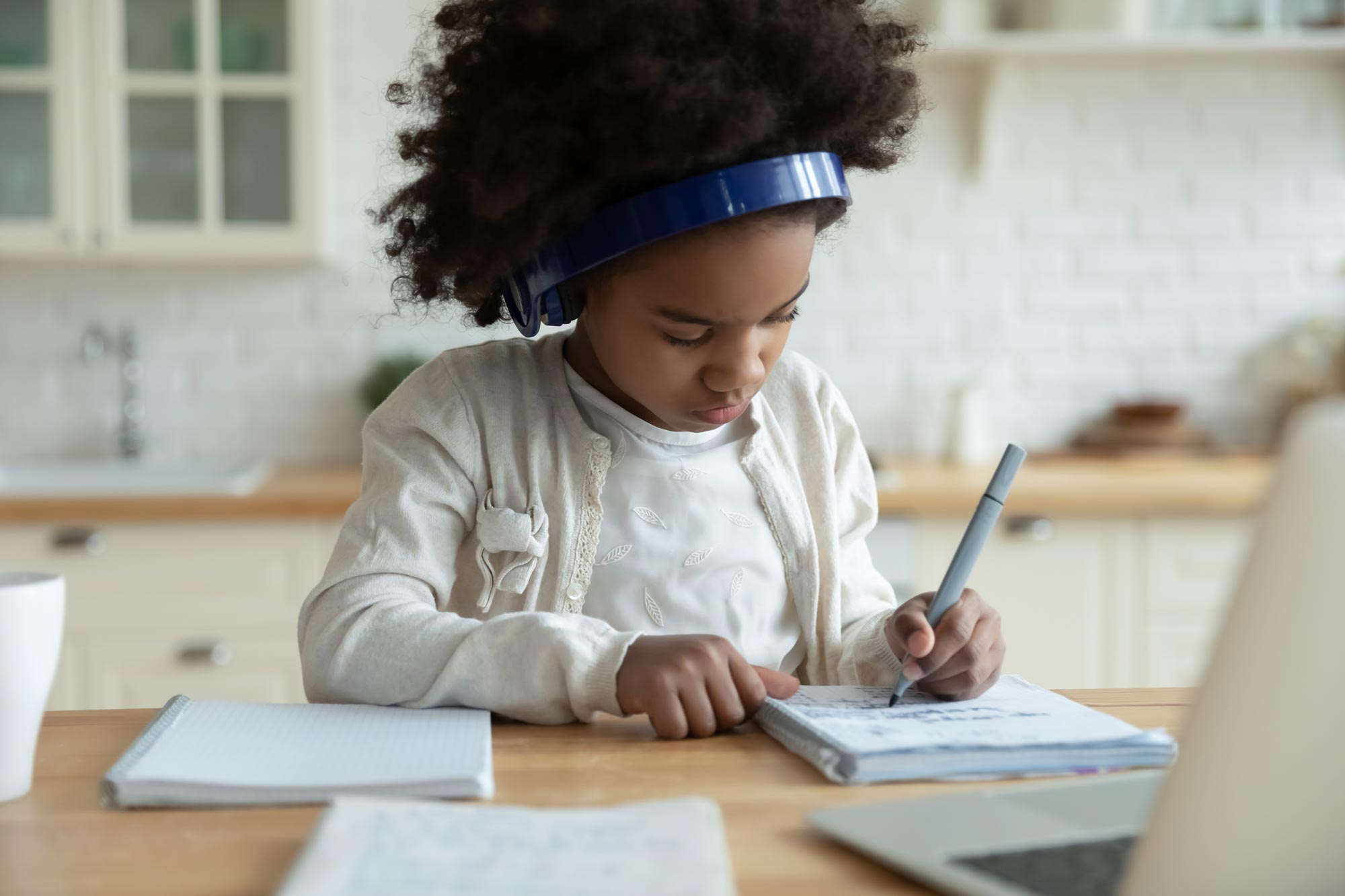 Child wearing headphones sitting at a table writing in a notebook