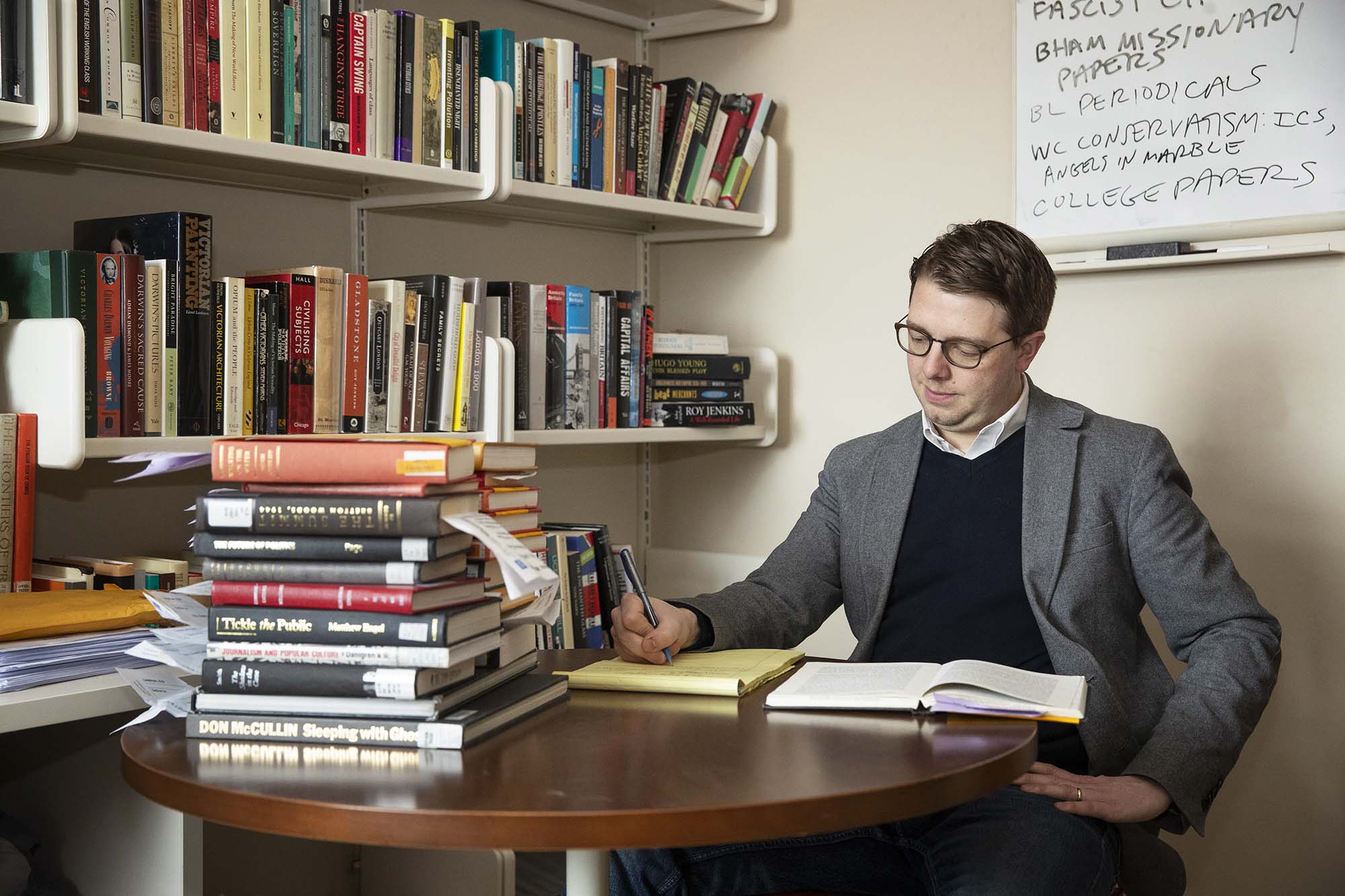 Erik Linstrum sitting at a table with a stack of books writing on a yellow notepad