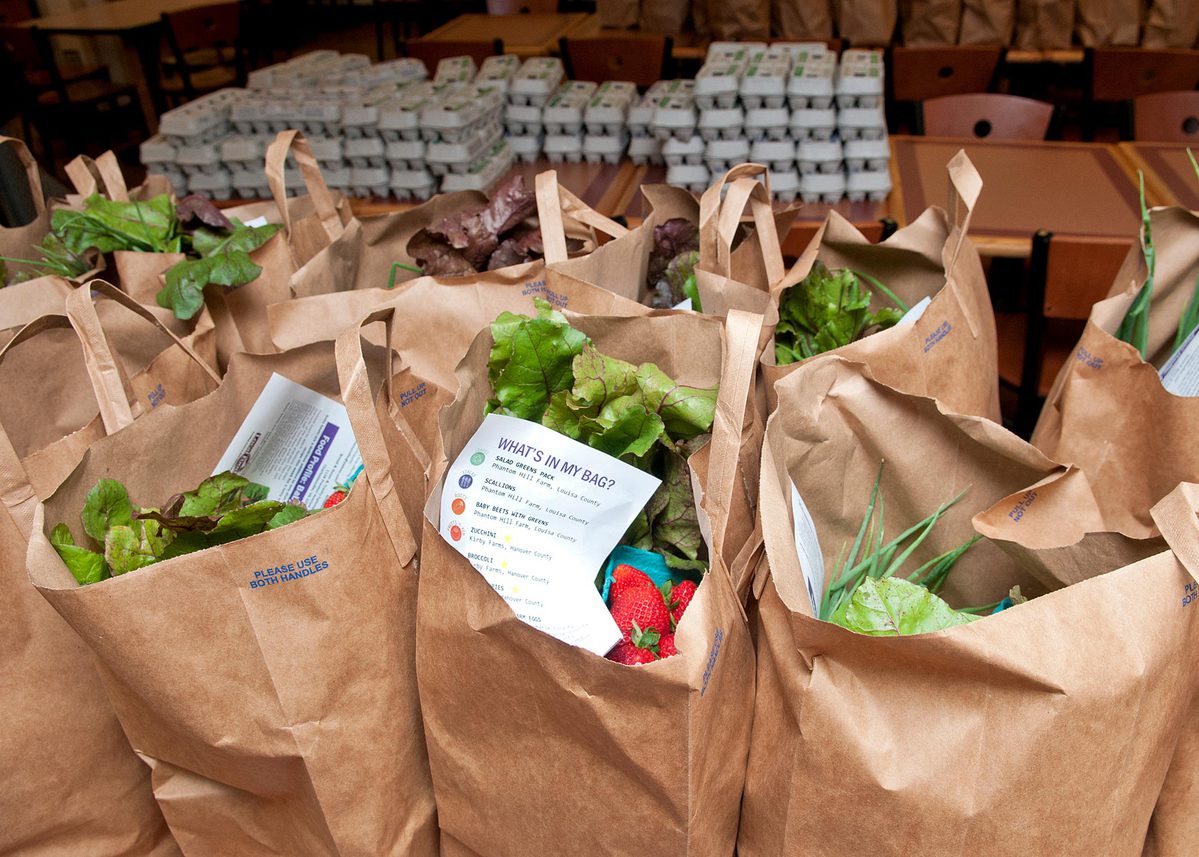 Brown paper bags filled with Vegetables and cartoons of eggs behind the bags on tables 