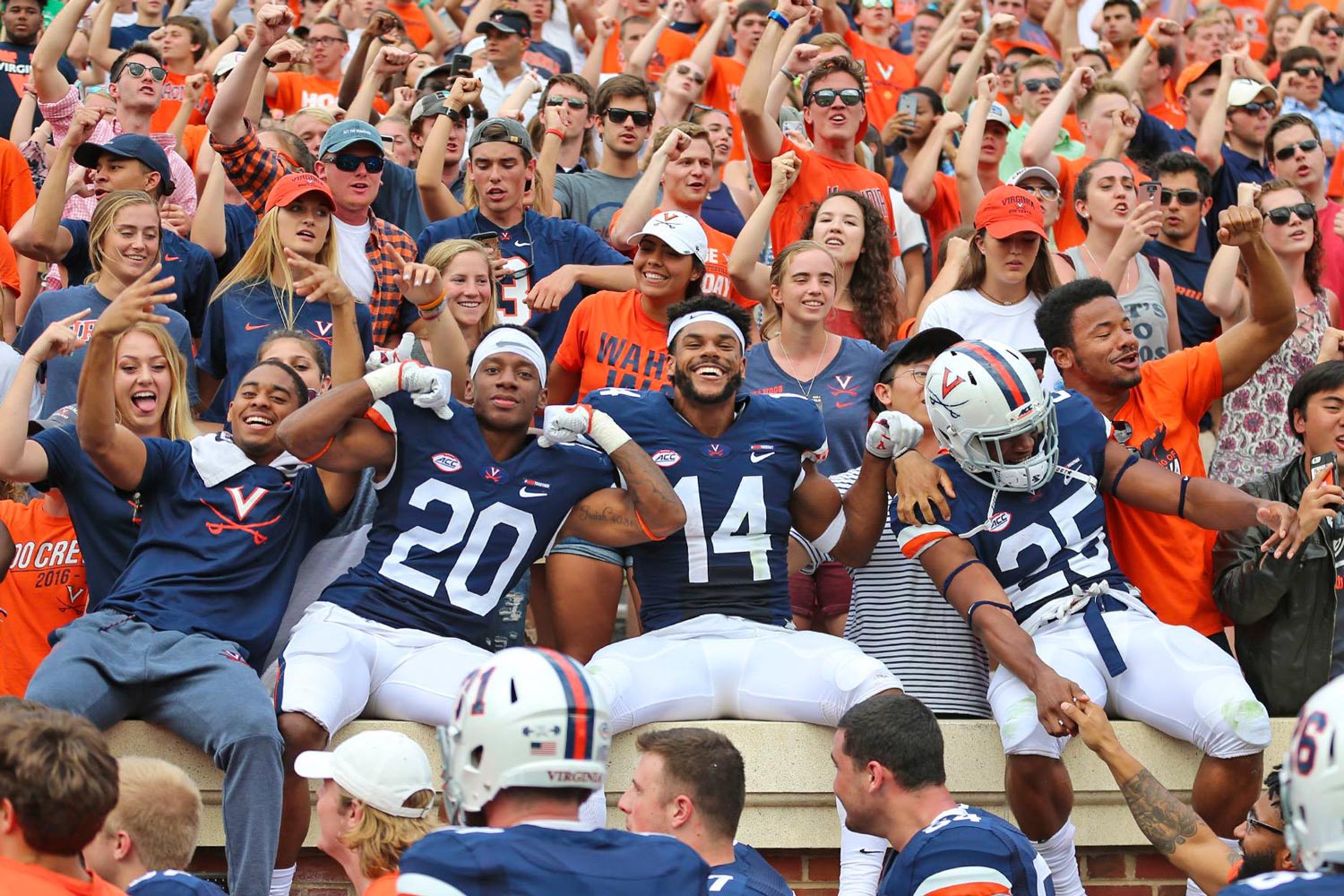Football players sit on the wall with fans cheering behind them