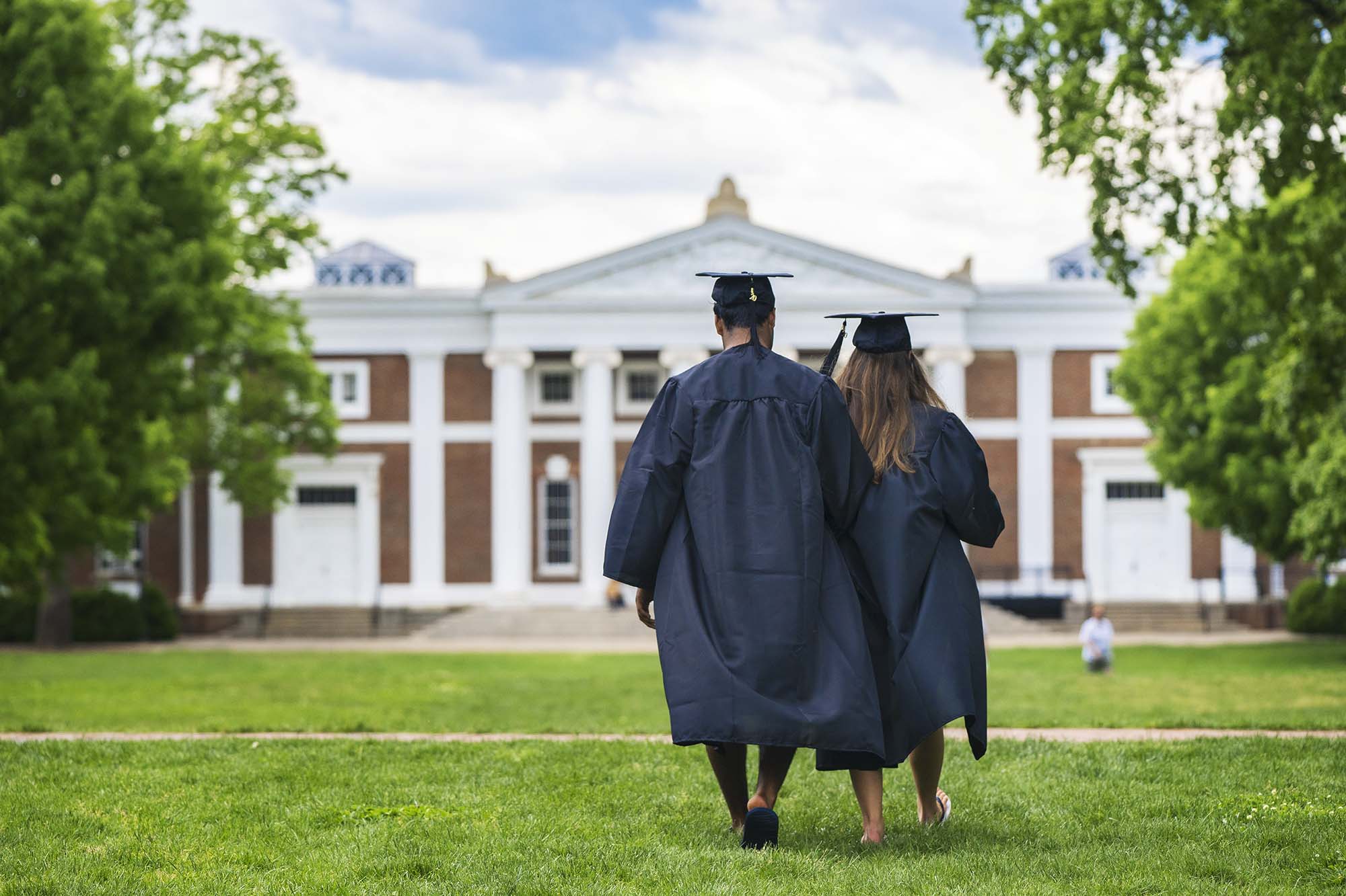 Two UVA Graduates walking across grounds in their caps and gowns