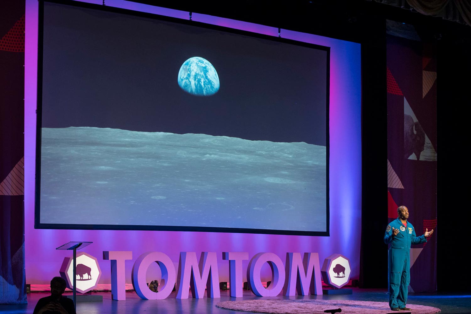 Melvin speaking on stage with the earth as seen from the moon on screen