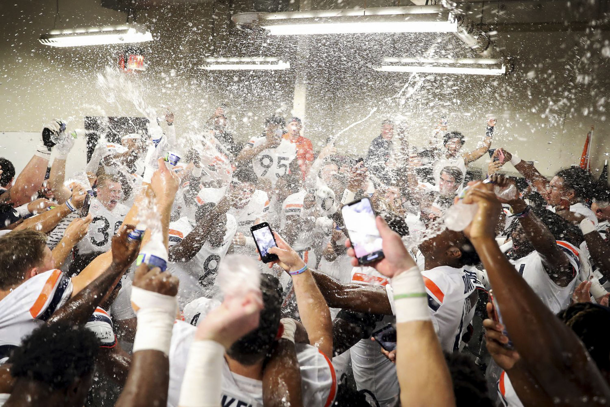 UVA Football team in locker room spraying water in the air after victory in Louisville