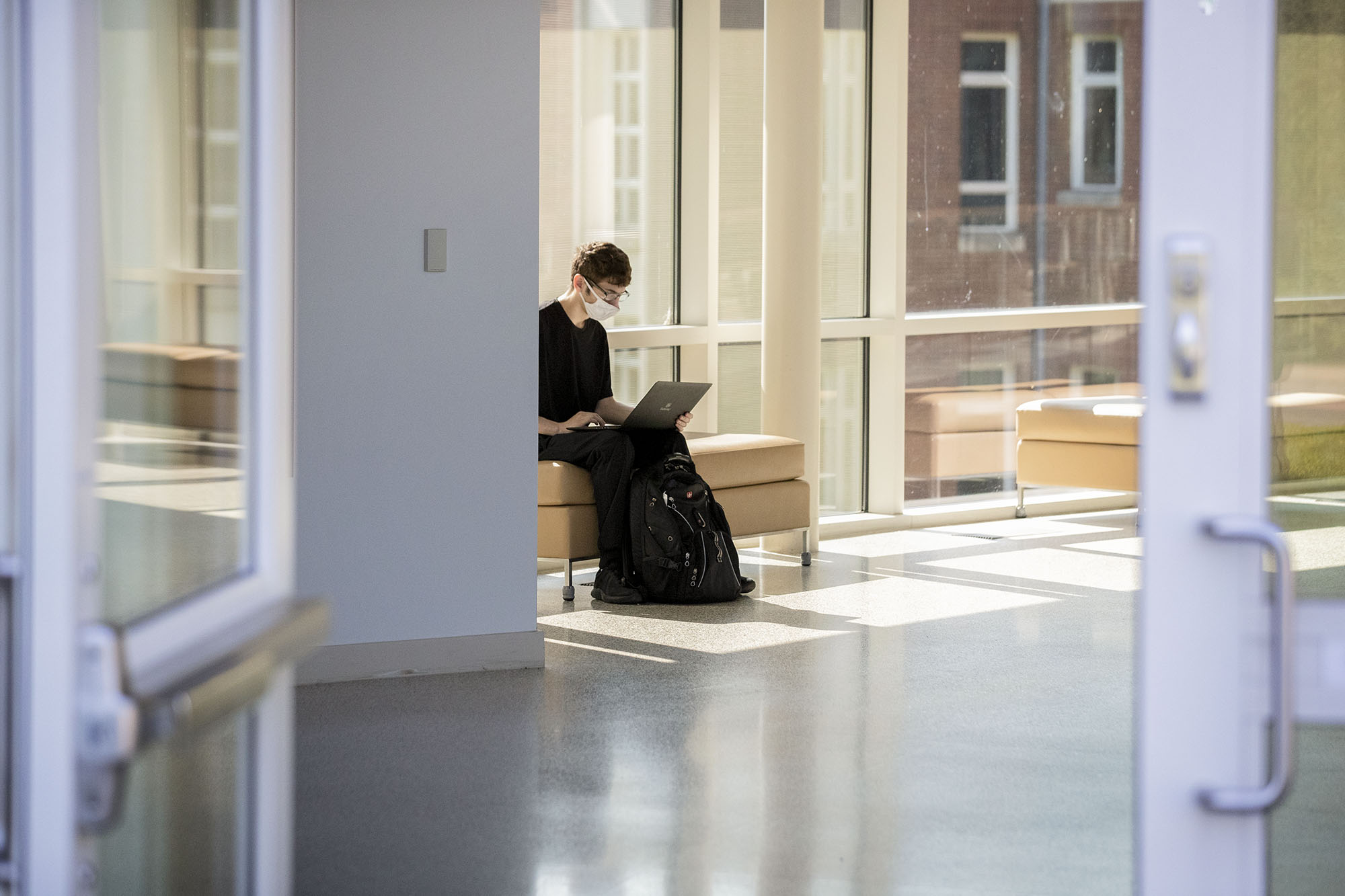 Student sitting in the hallway on a sofa working on their computer