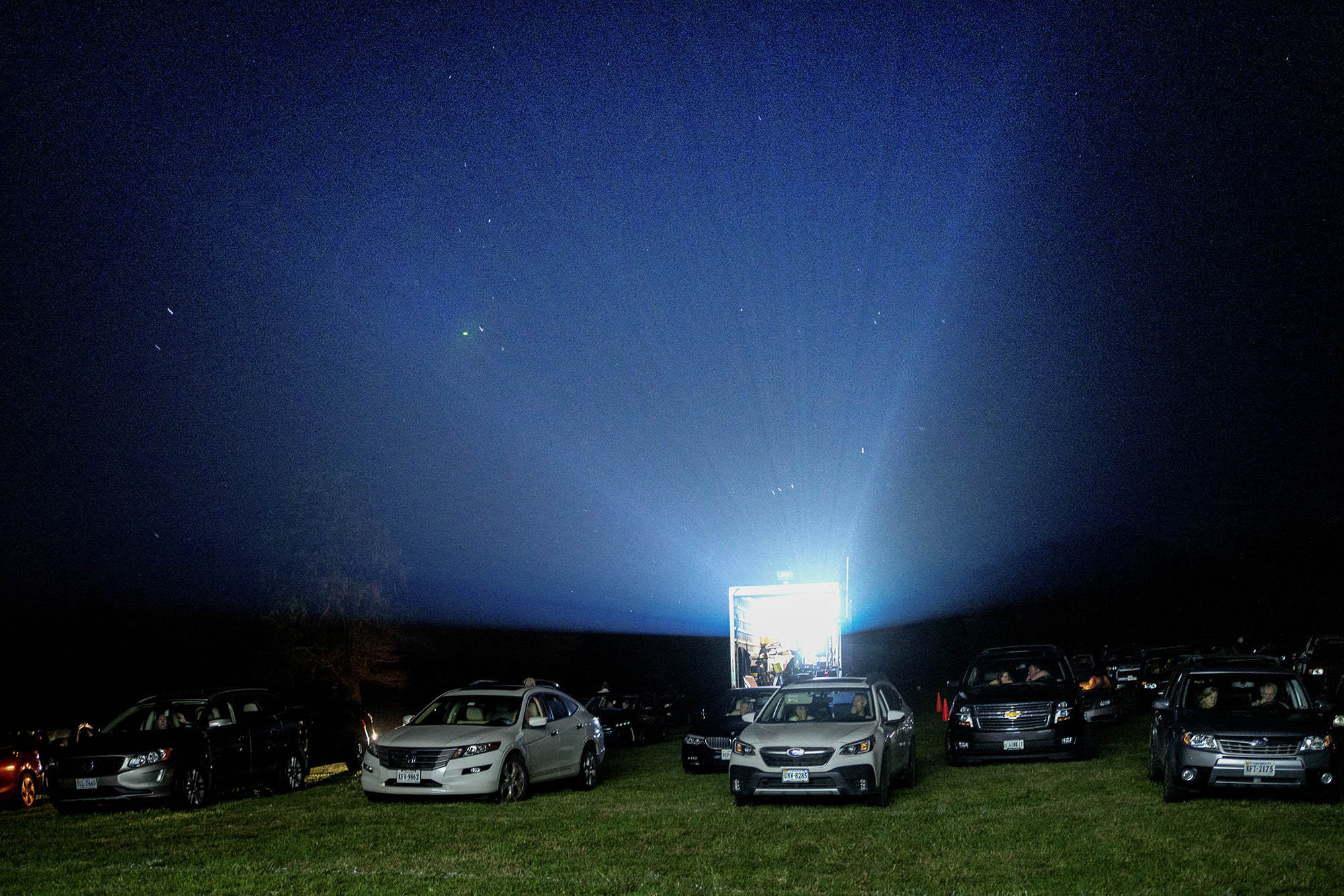 Vehicles lined up in a field as the drive-in movie projector shines bright out of a trailer 