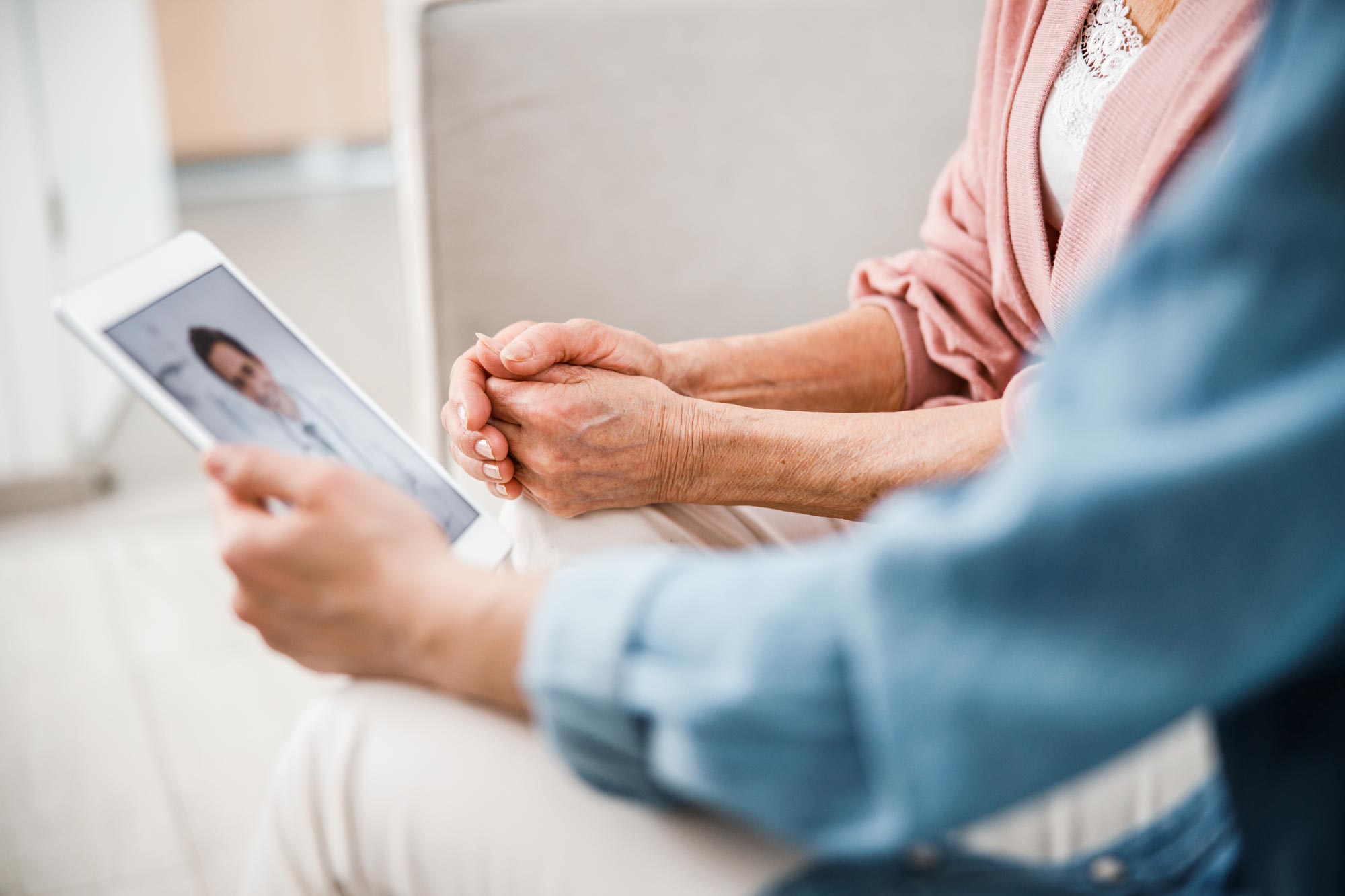 Two people sitting together speaking to a doctor on their tablet