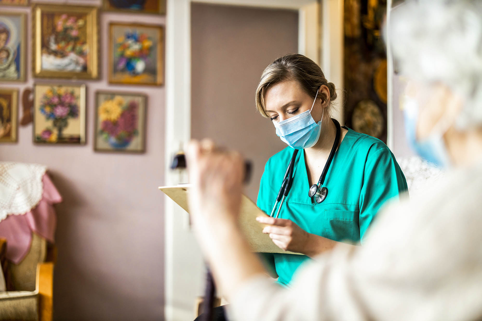 Nurse writing her clipboard while working with an elder adult