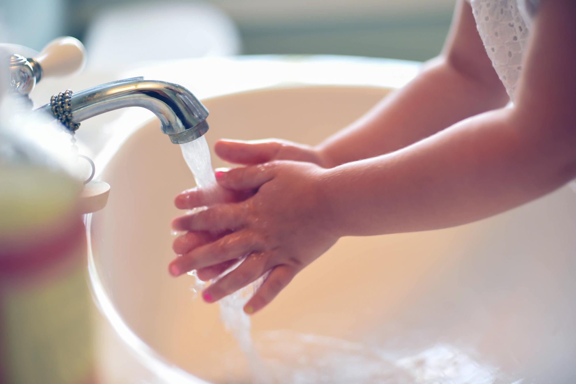 Little kid washing their hands in a white sink