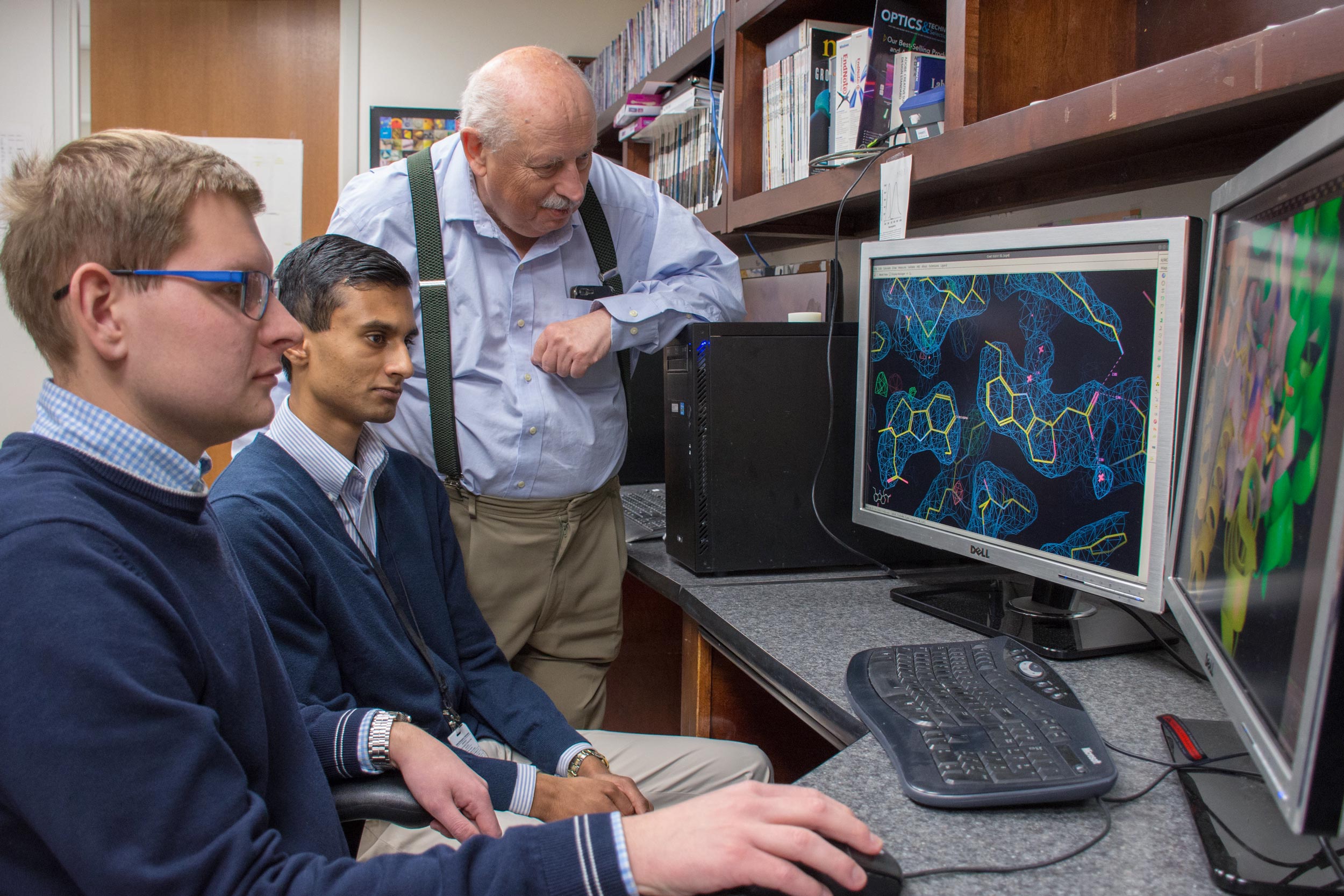 Graduate student Mateusz Czub, left, and undergraduate chemistry student Barat Venkataramany, center, analyze a testosterone binding site and discuss the possible medical implications of their finding with Wladek Minor. 