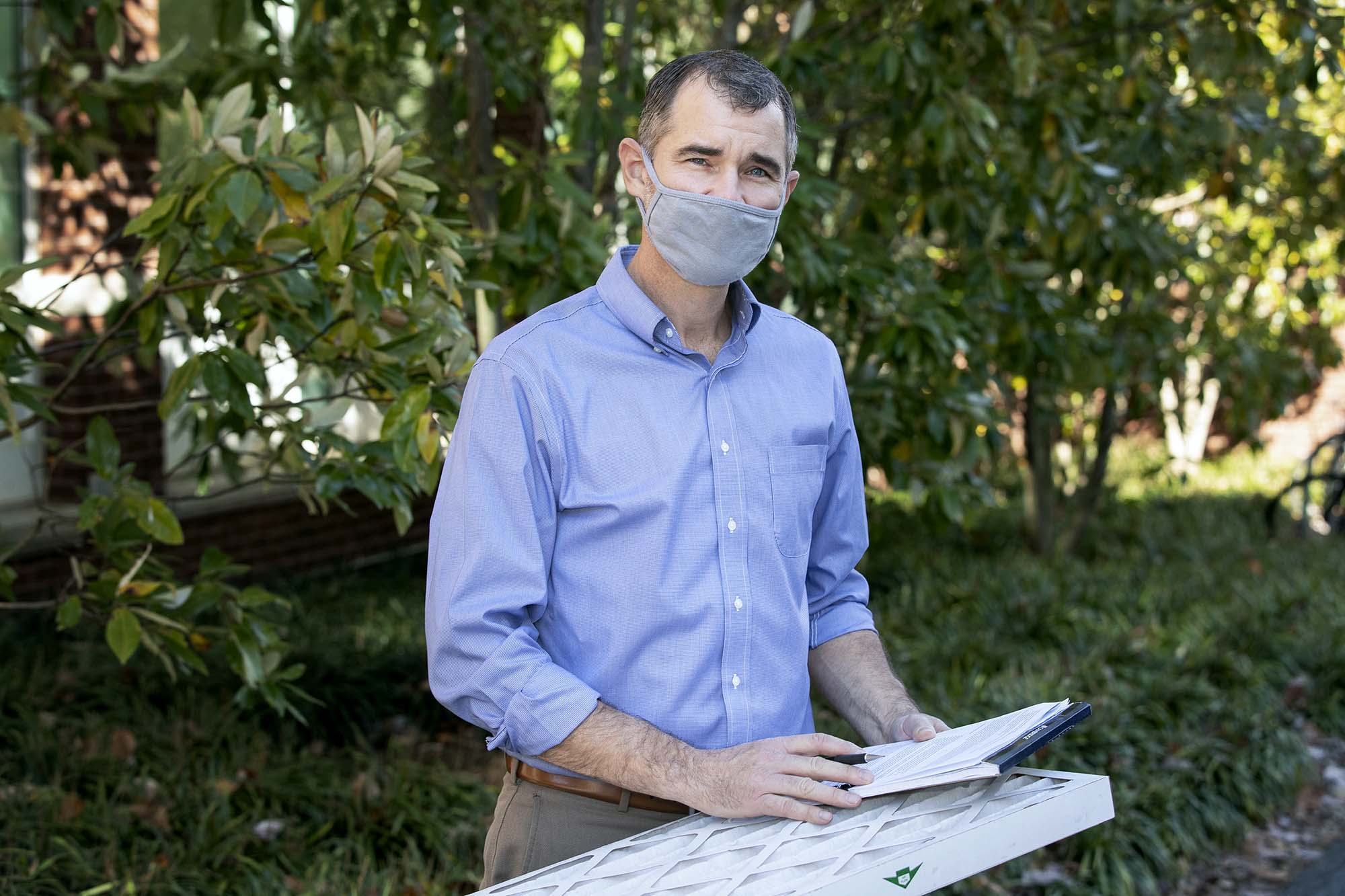 Roland Zumbrunn stands while holding an air filter and notepad