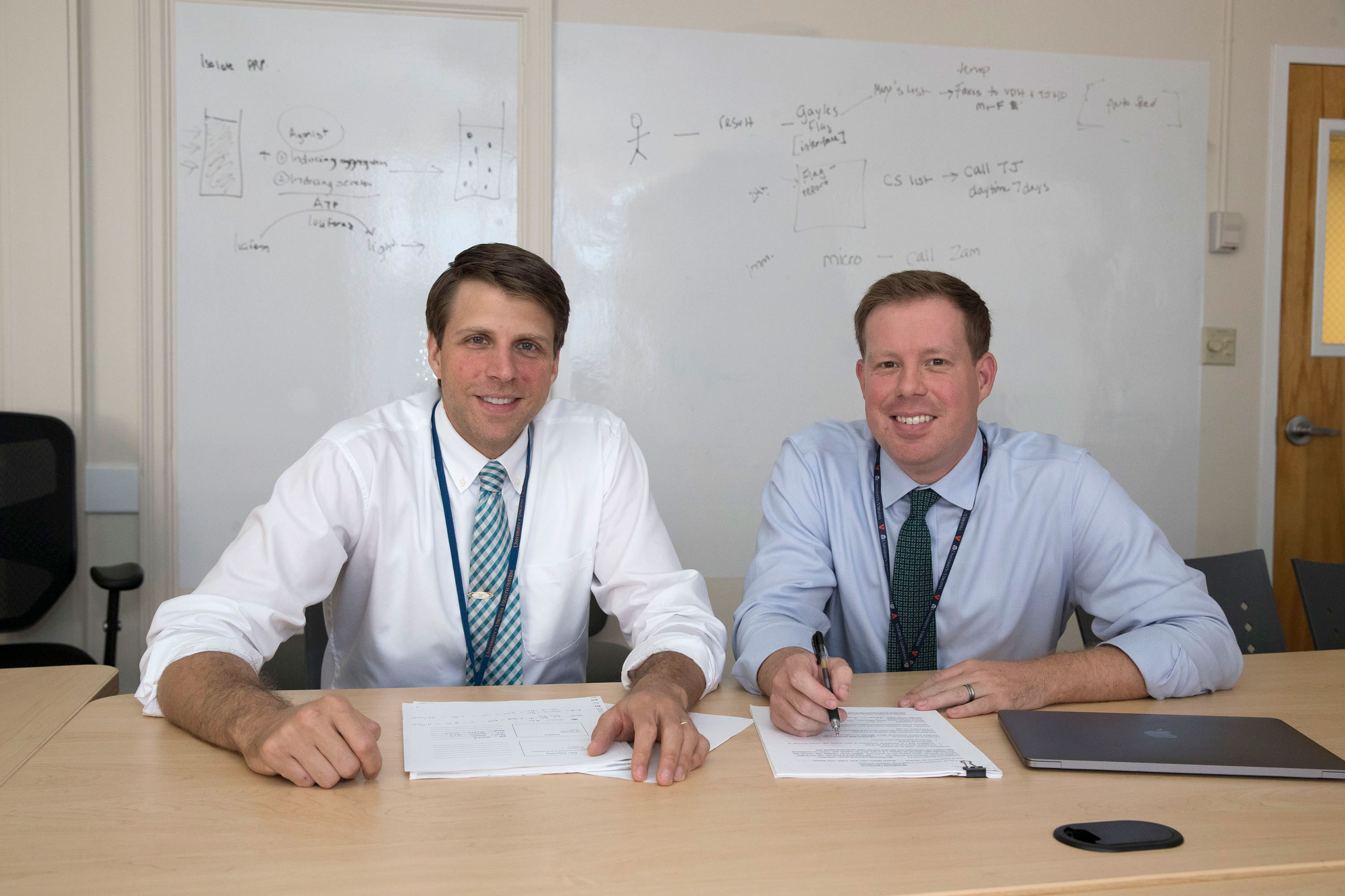 Joseph Wiencek, left, and Andrew Parsons, sit at a table working at papers together looking at the camera