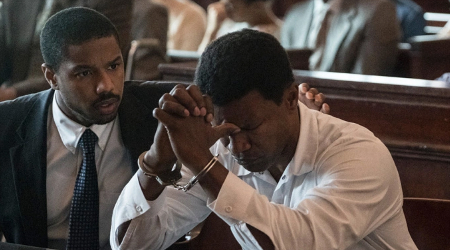 Still frame from the movie Just mercy.  A black attorney comforts his client who is sitting in handcuffs with their head on their hands