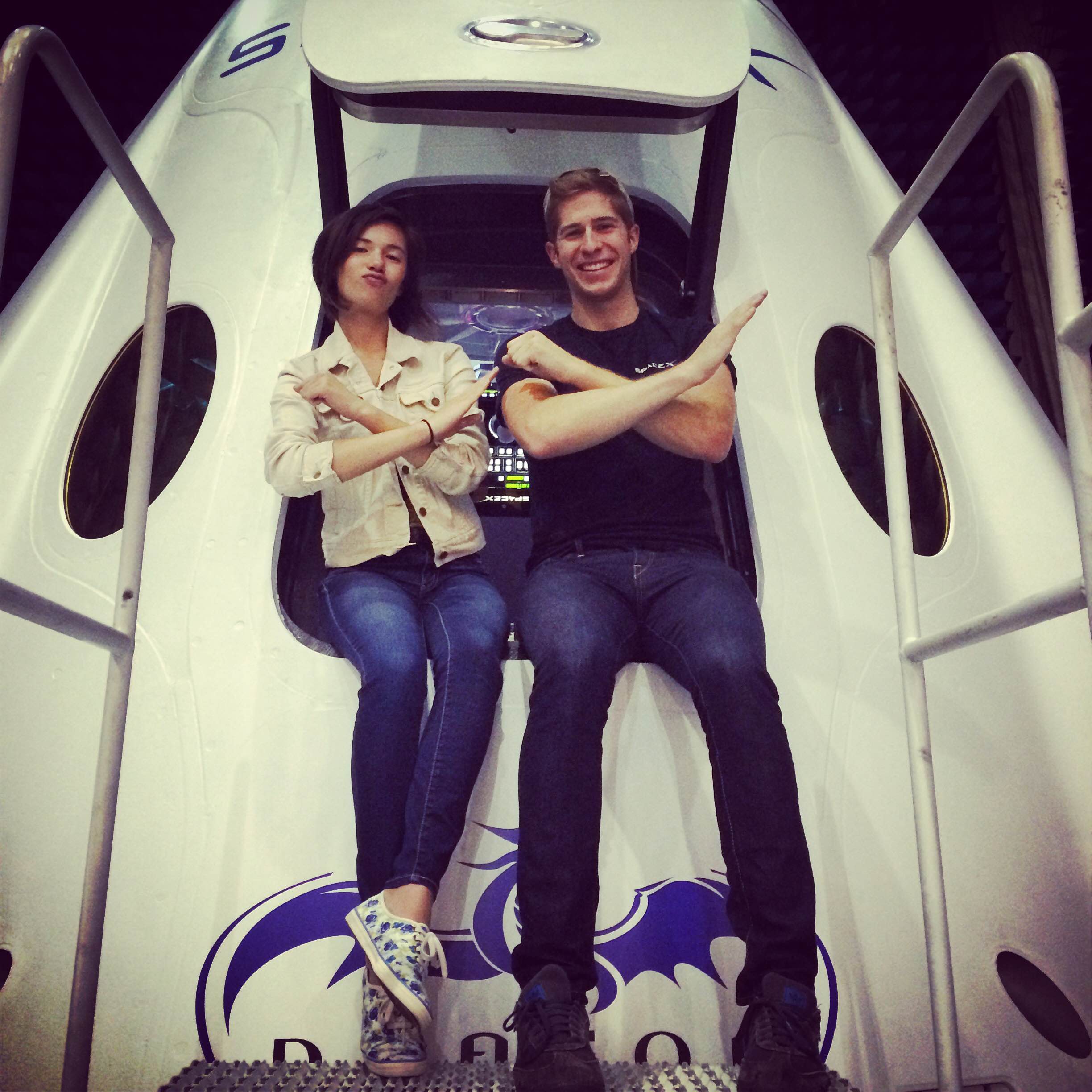 Kelly Thomas, left, and a SpaceX colleague making the spaceX sign with their arms and sitting on the entrance of the spaceX craft