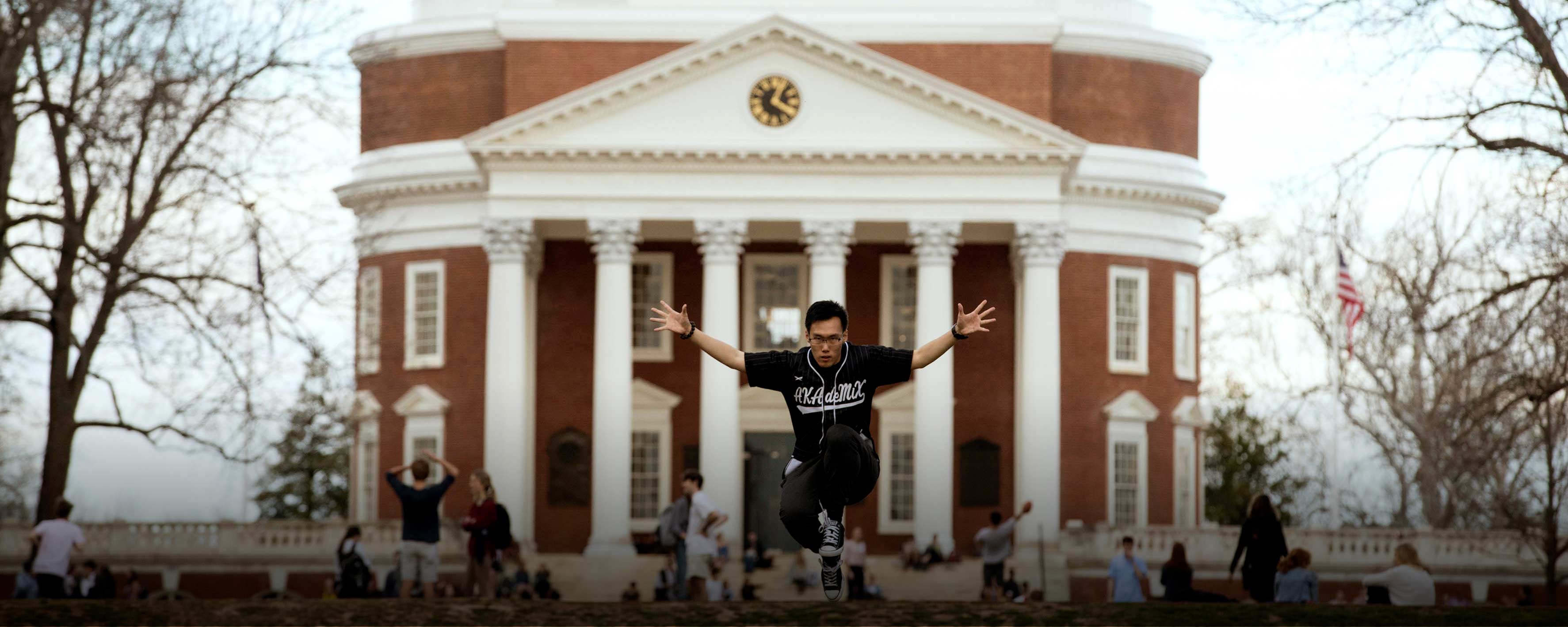 Man jumping with his hands out wide looking at the camera in front of the Rotunda