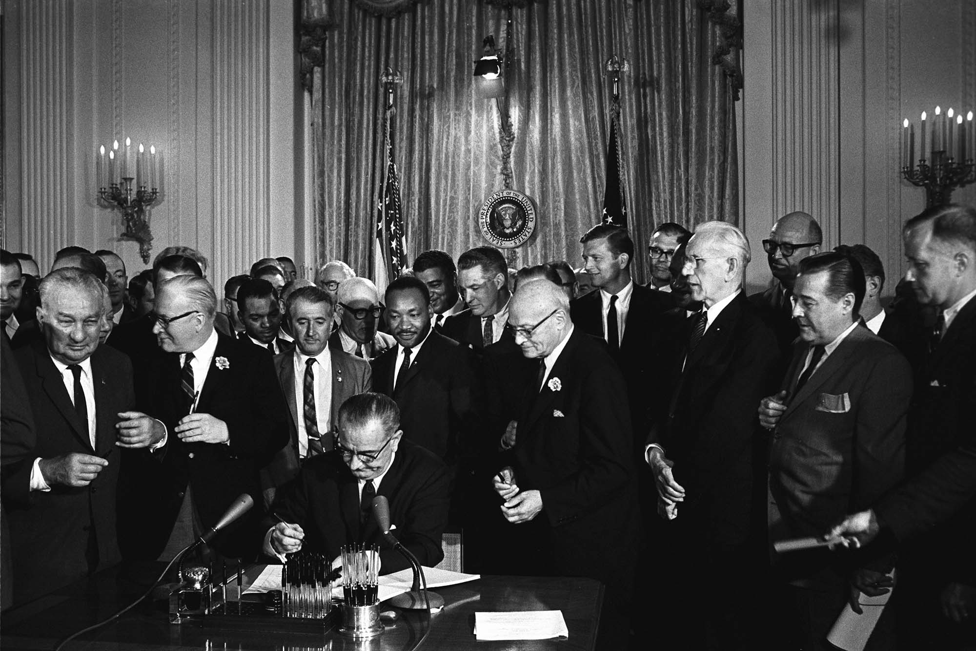 President Lyndon B. Johnson signs sitting at a table signing the 1964 Civil Rights Act