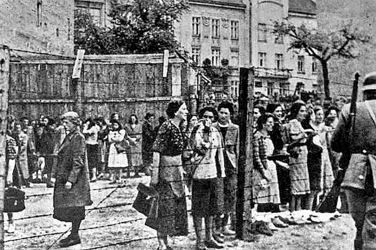 Jewish residents pictured inside the Lviv ghetto talking to soldiers from inside a fence. black and white image
