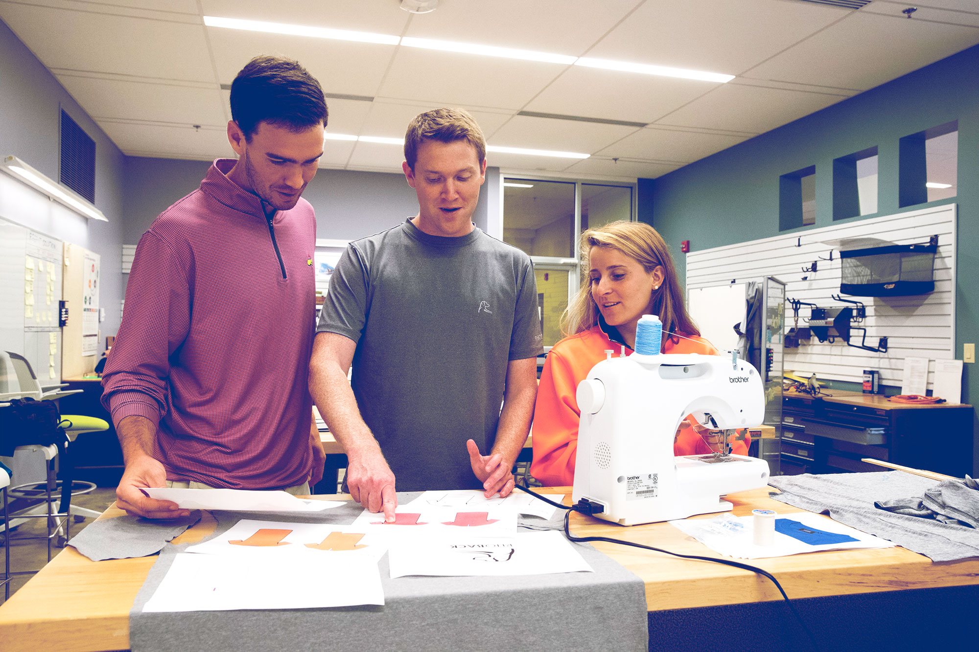 Matt Loftus, left, business partner Kevin Hubbard, middle, and Kristina Loftus, right, stand at a table looking at shirt designs