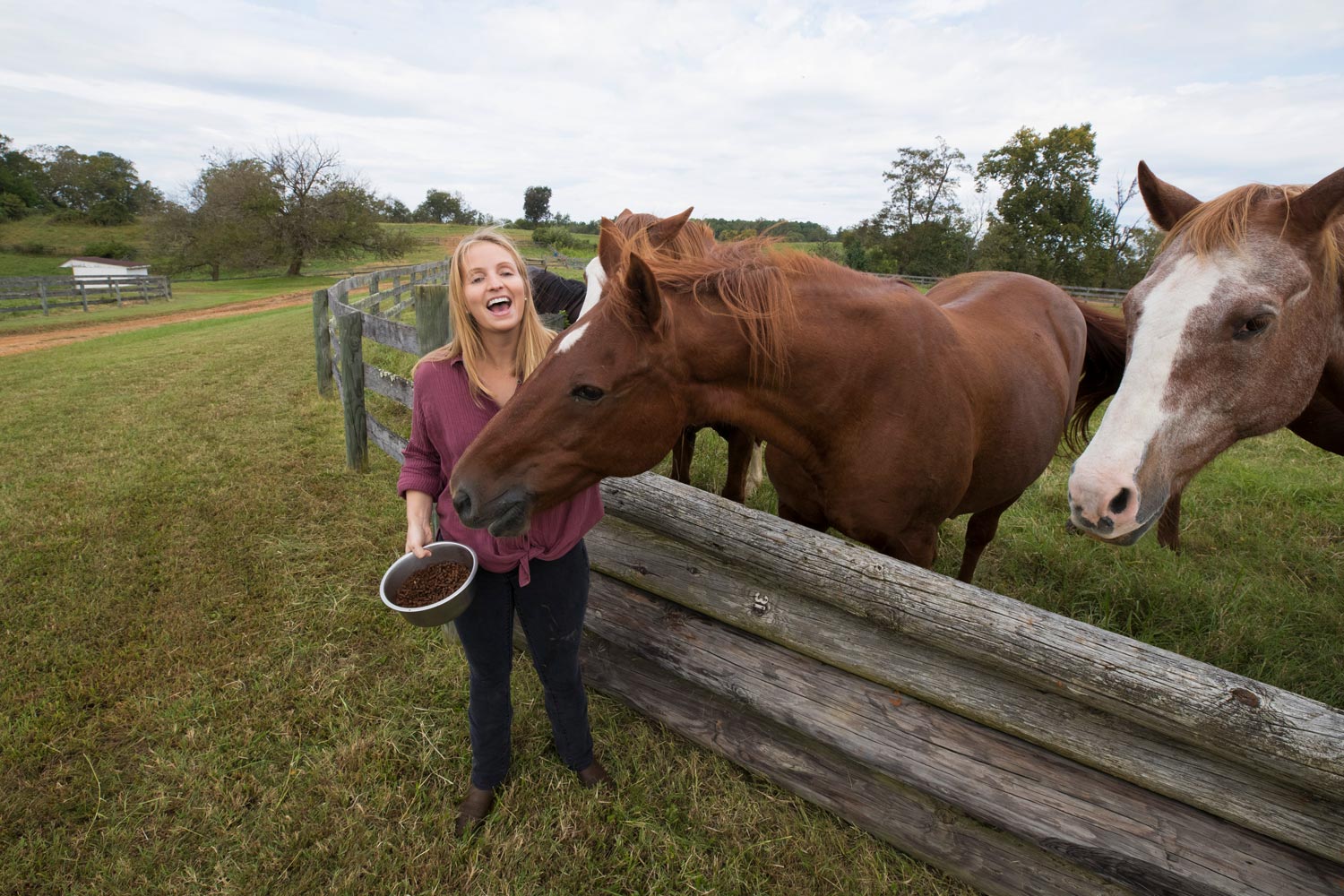 Meg Greenhalgh feeds horses over a wooden fence