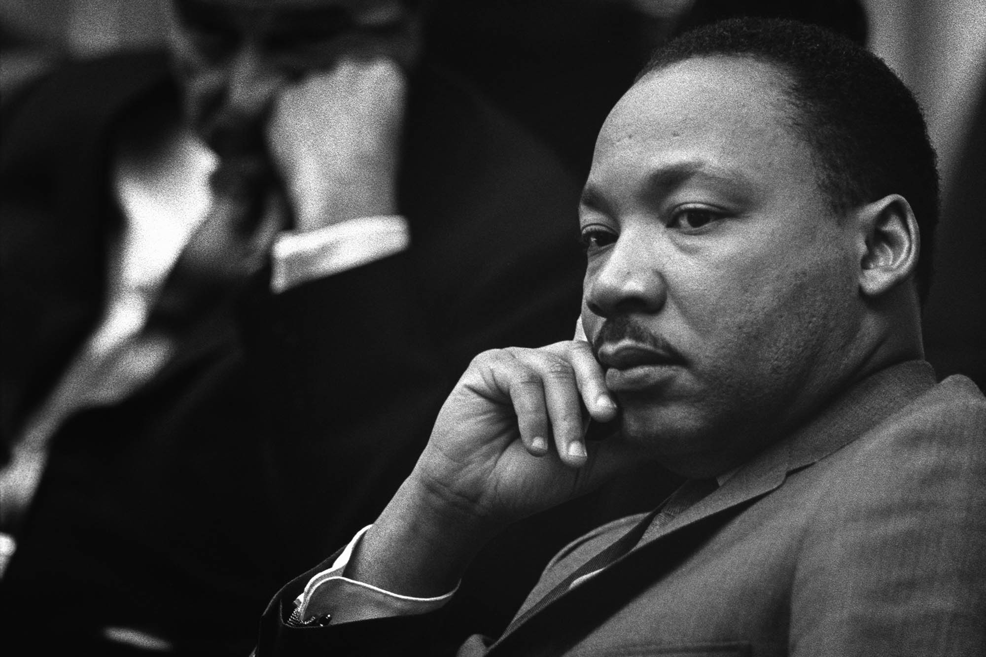 Rev. Martin Luther King Jr.sitting in a chair looking to the left at someone speaking