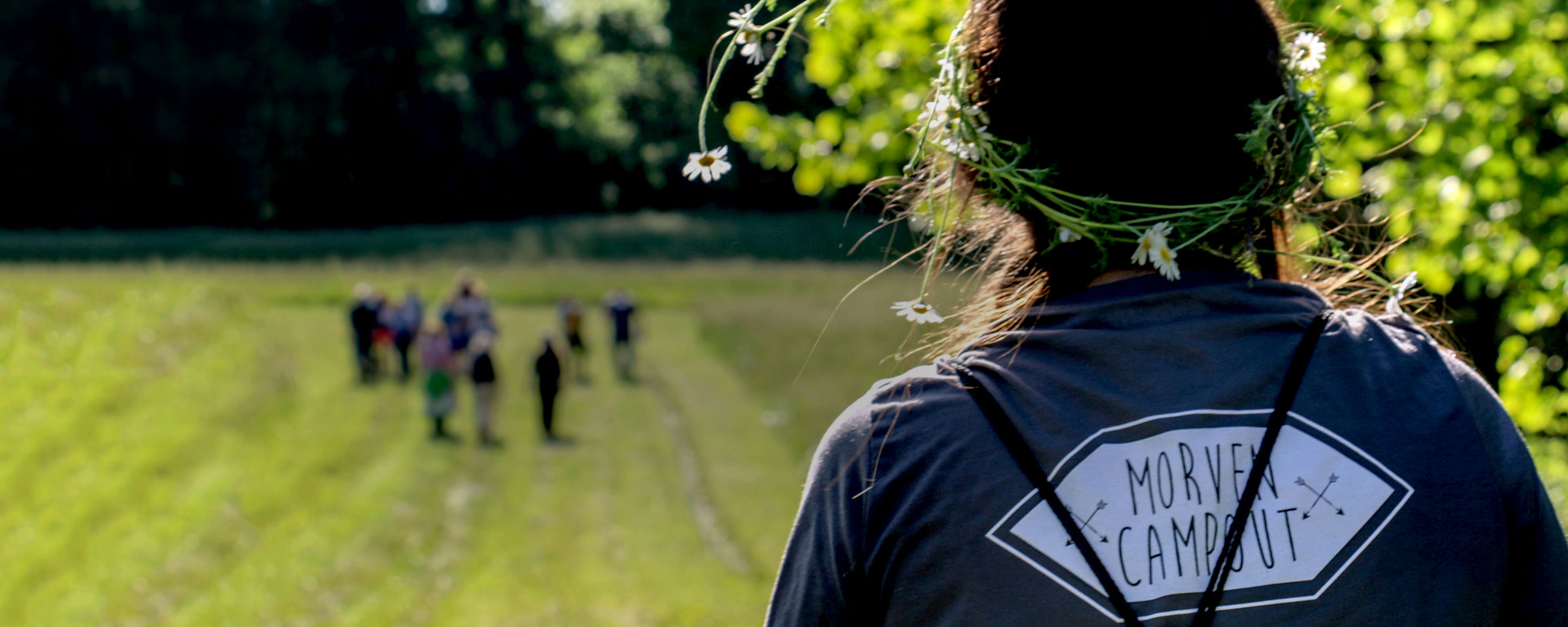 Person standing watching people in a field.  The back of their shirt says Morven Camps