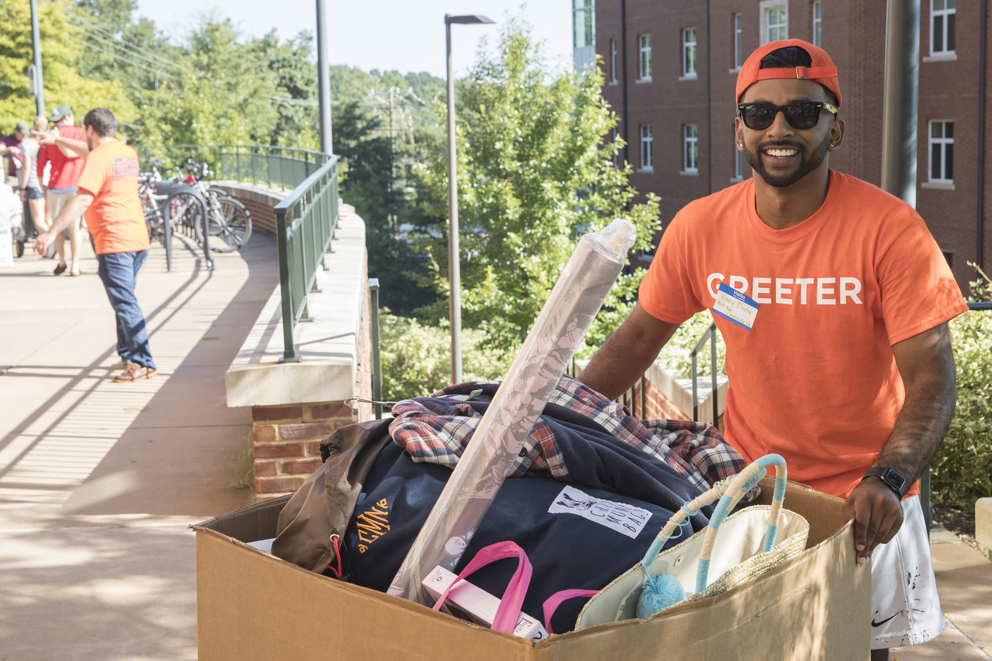 Greeter in a bright orange shirt helps move a box of students belongings up a sidewalk