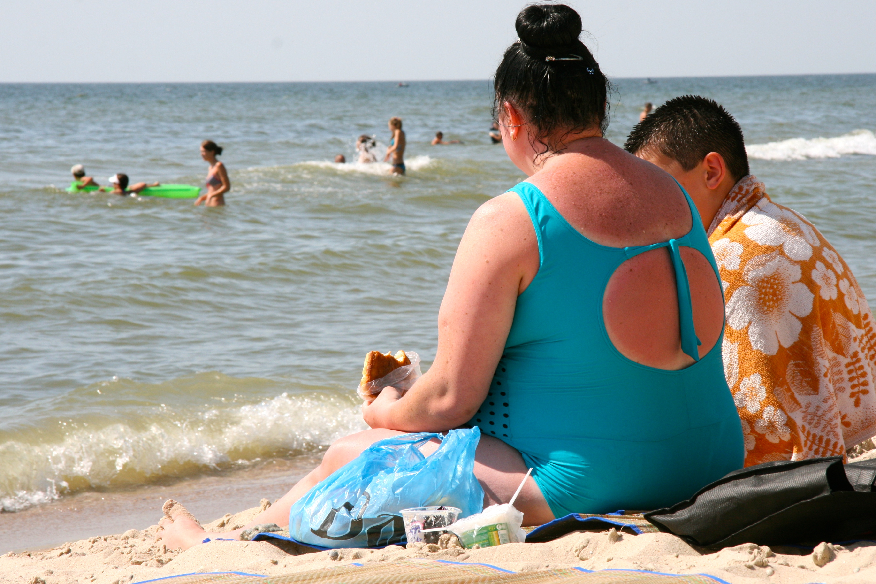 people sitting on the beach eating while people are in the ocean 