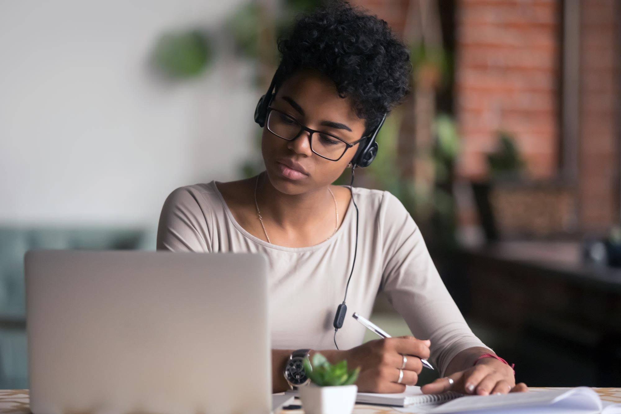 Woman sitting at a table writing in a notebook while looking at her laptop