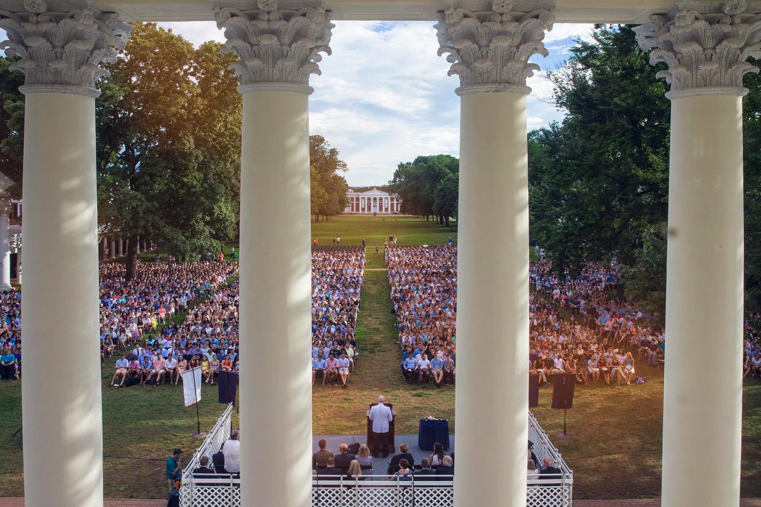 Man speaking at a podium to a crowd of students sitting on the lawn in chairs
