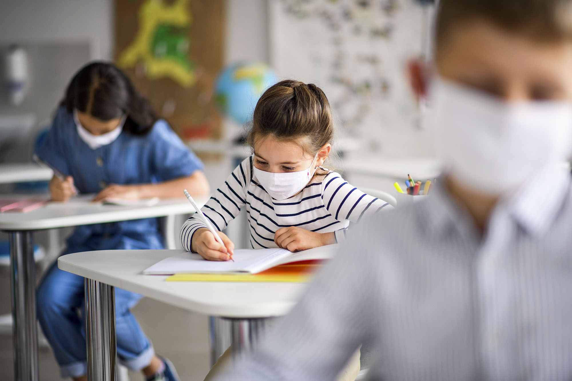 Children in class writing in notebooks socially distanced wearing masks