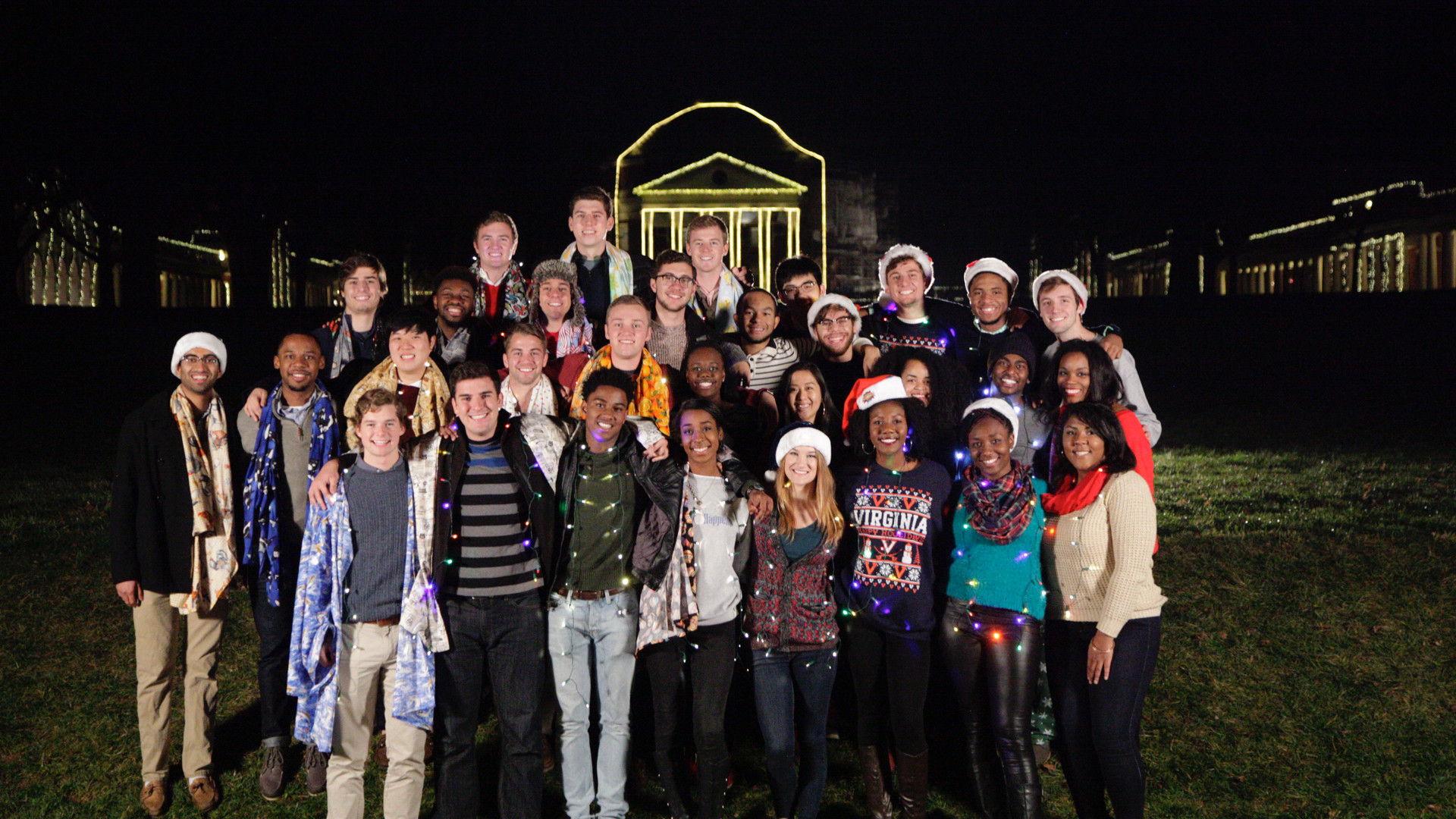 Group photo of students decked out in Holiday lights and attired with the Rotunda behind them outlined in lights