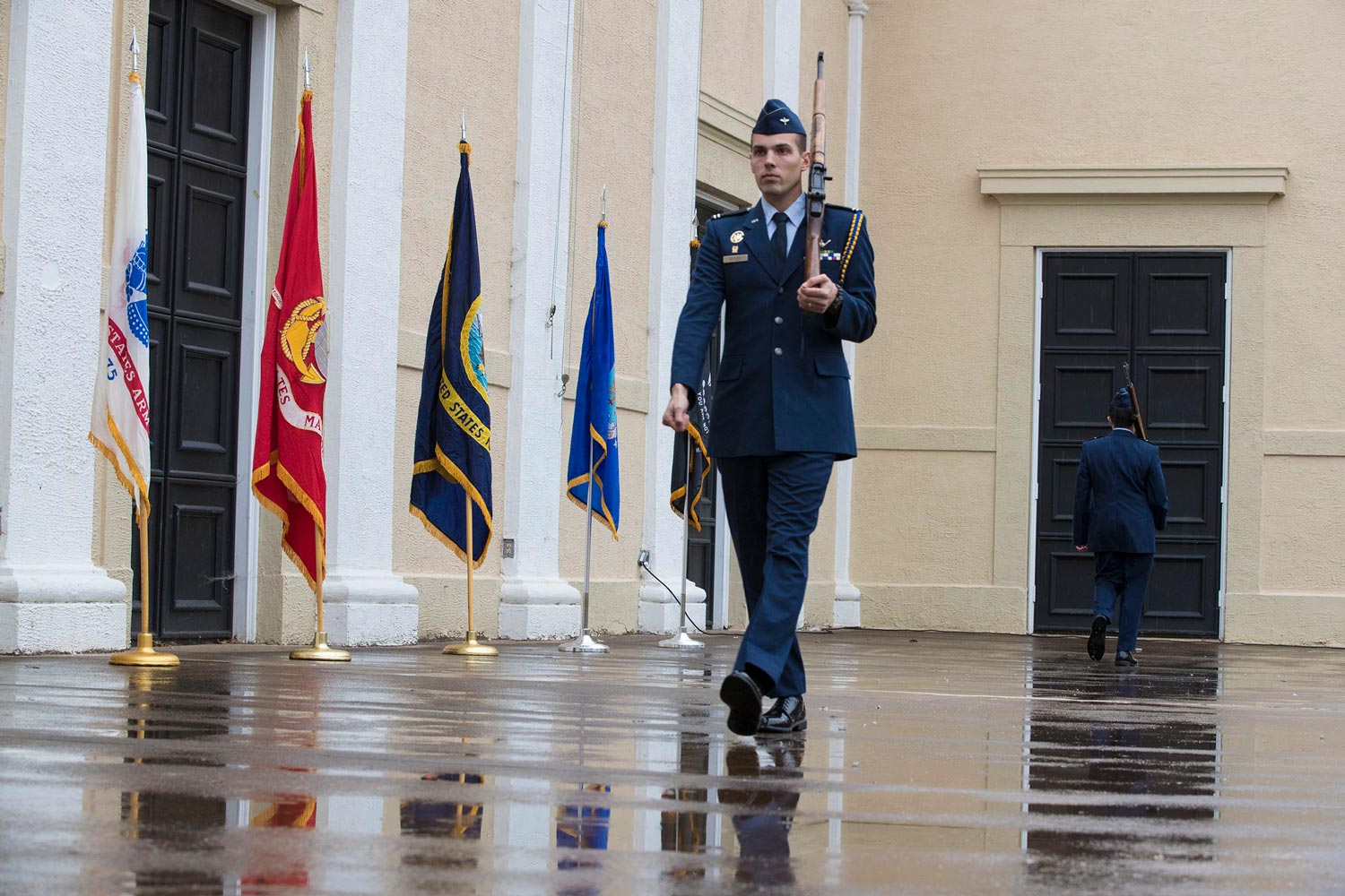 UVA ROTC student marching with rifle in front of US Armed forces flags