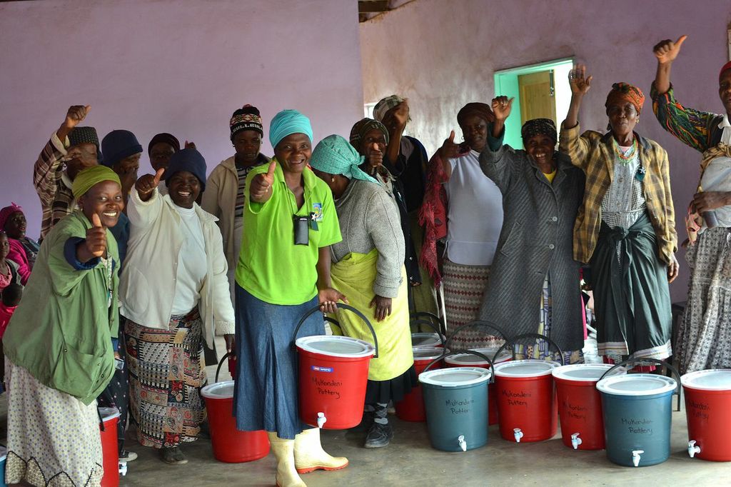 Women from South Africa stand together holding buckets of clean water giving the camera a thumbs up