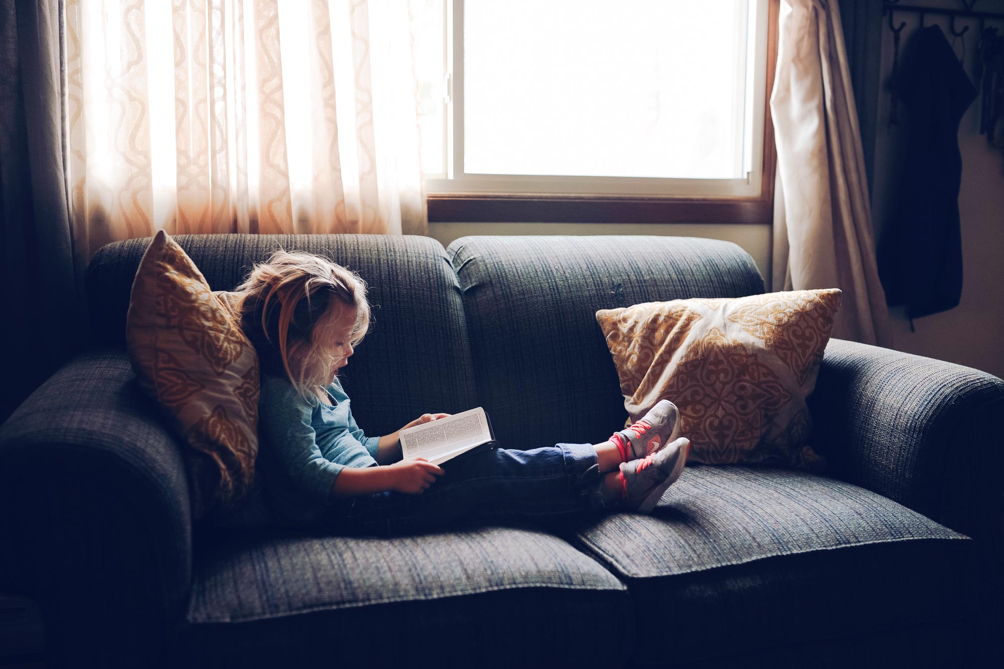 Little child sits on a couch reading a book