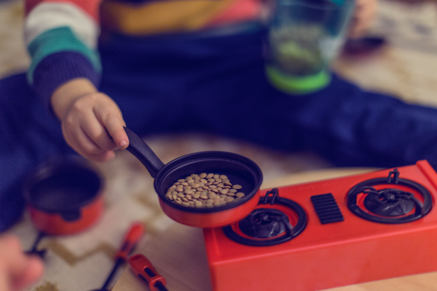 Small child's hand holding a toy pot filled with lentils