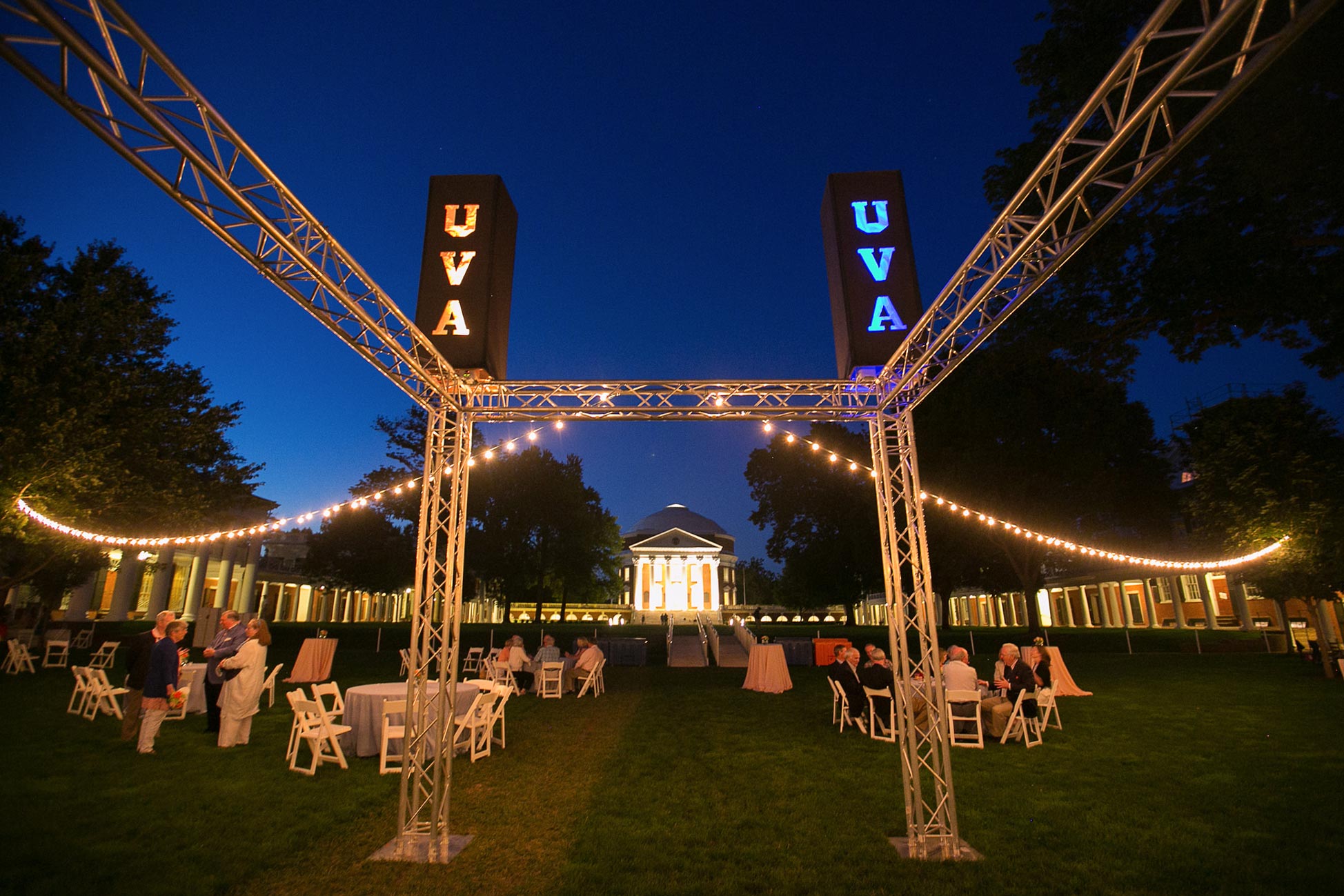 Tables on the lawn with a metal structure that hold lights that say UVA