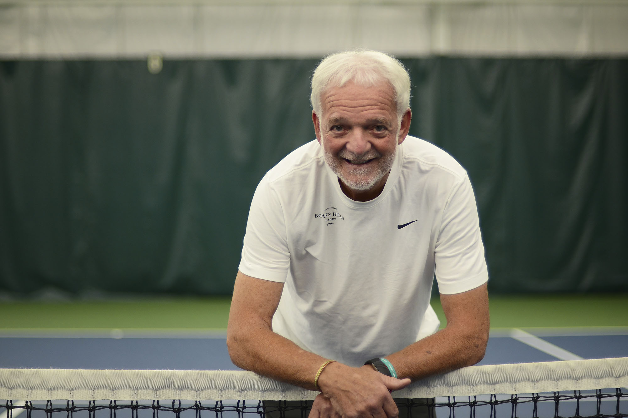 Ron Manilla’s headshot of him leaning on a tennis net