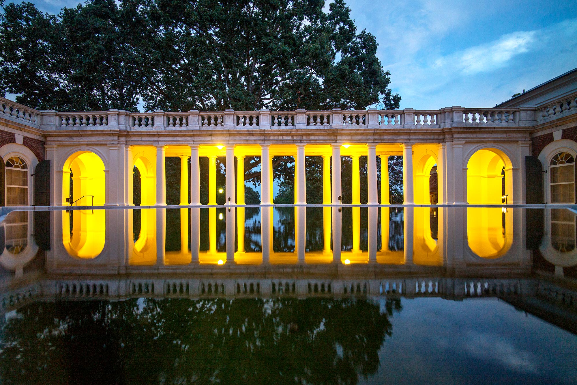 columned sidewalk lit up by lights reflecting off of a reflection pond