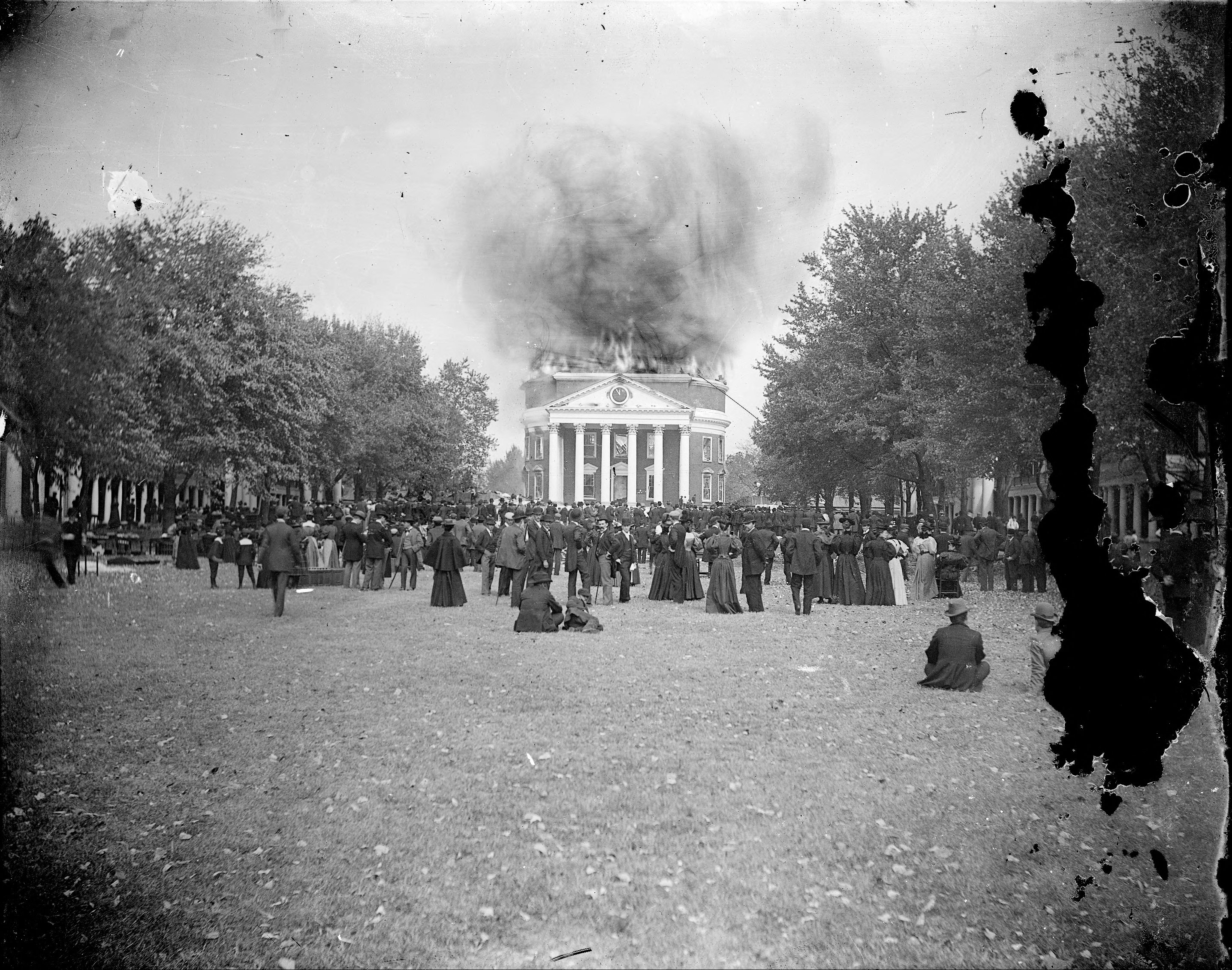 Smoke rising from the Rotunda dome during a fire. The lawn is packed with onlookers 