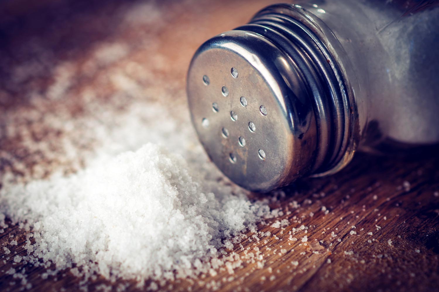 Salt piled on a table with a salt shaker on its side.