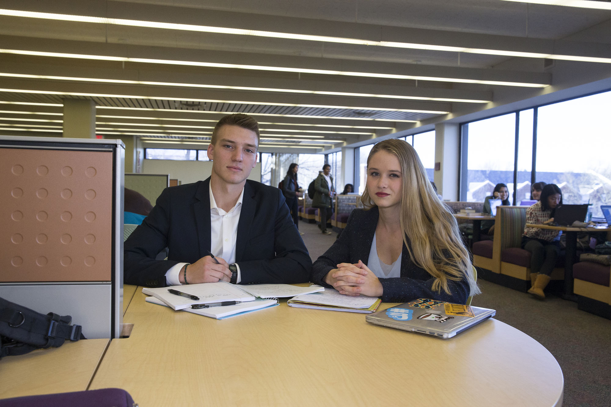 Orion Williams, left, and Sarah Koch sit at a table with notebooks smiling at the camera