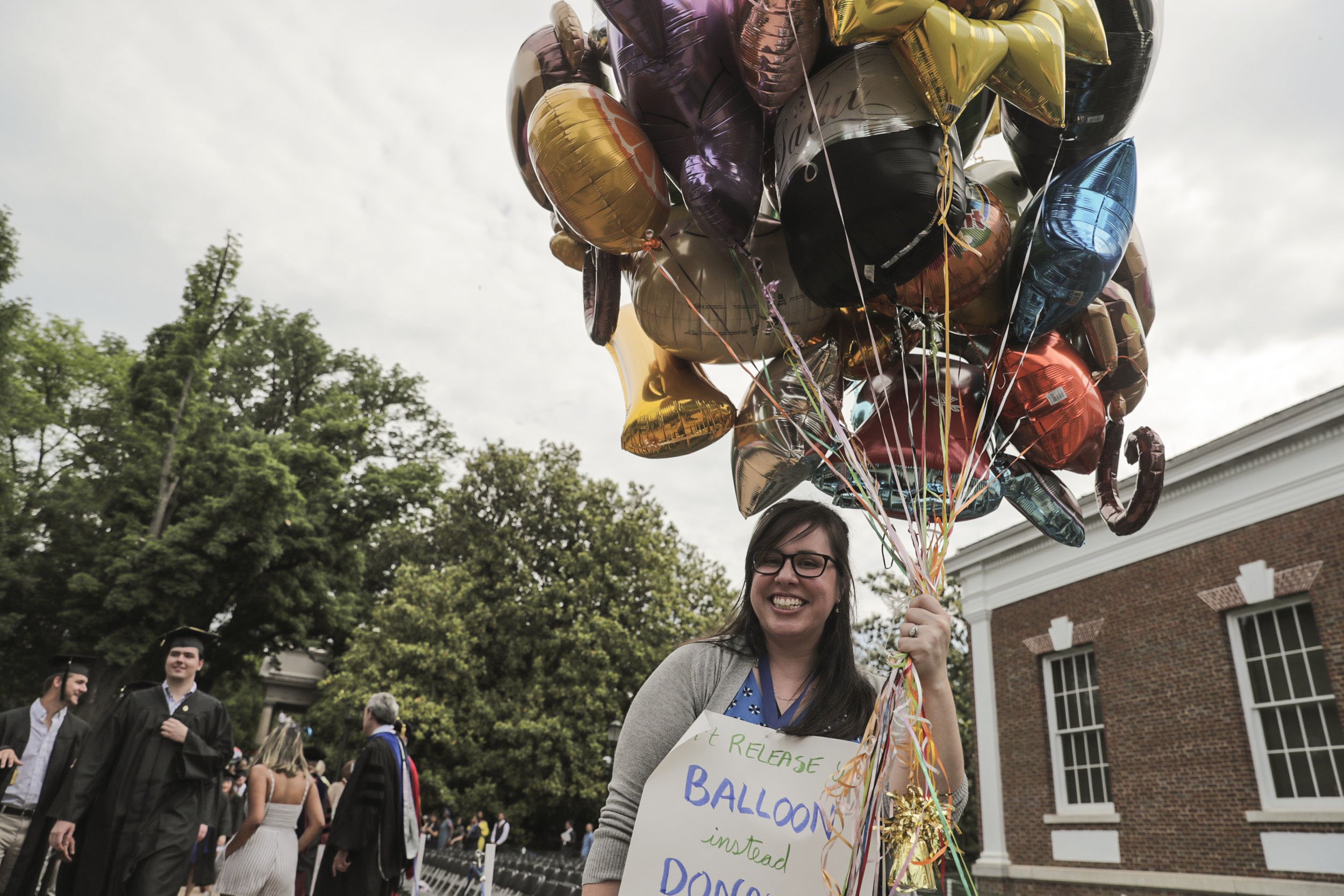 Woman holding balloons wearing a sign that reads: don't release balloons instead donate them