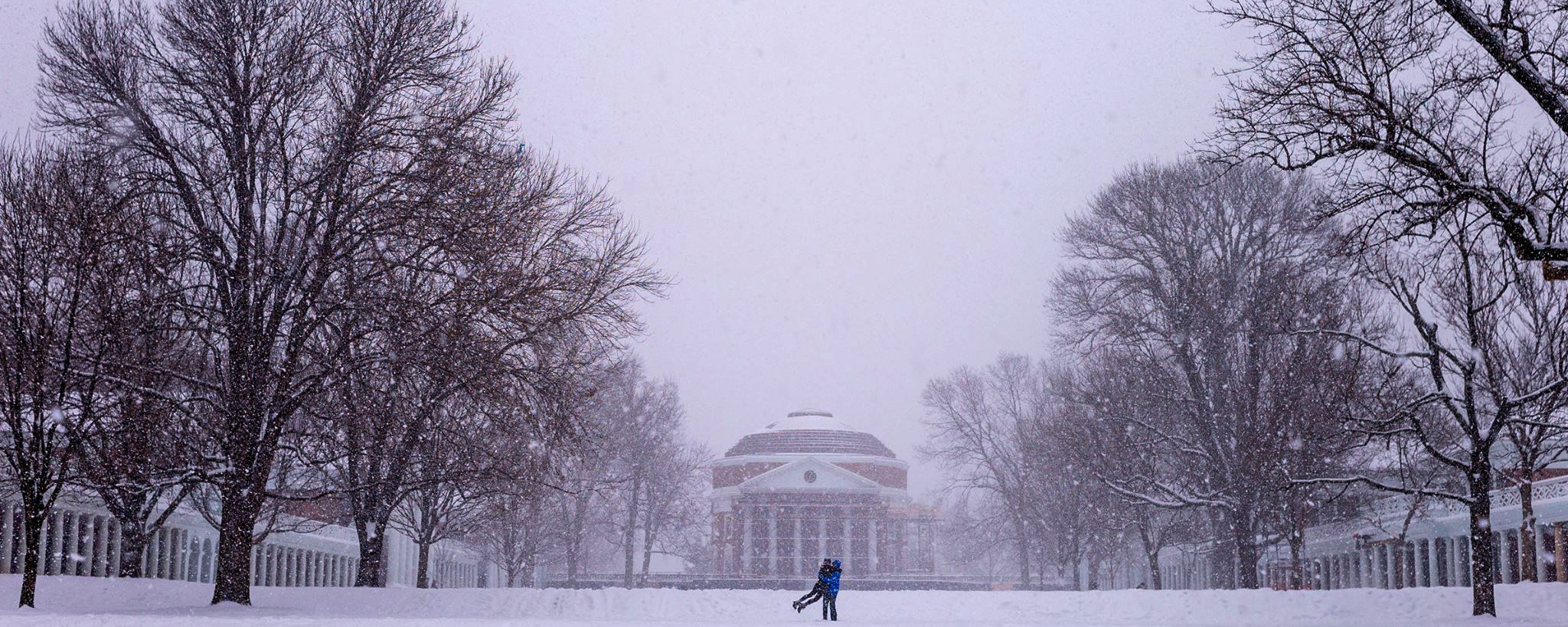 The Rotunda in the snow with two people playing on the lawn