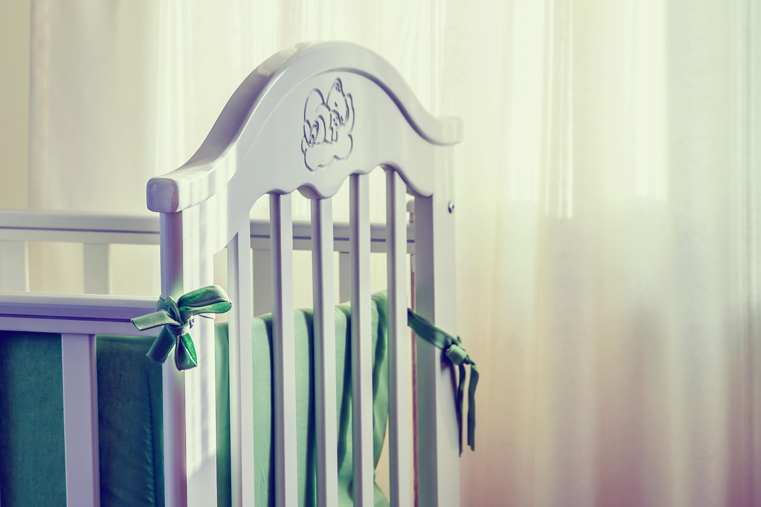 Baby crib with green ribbon holding up the inner pad